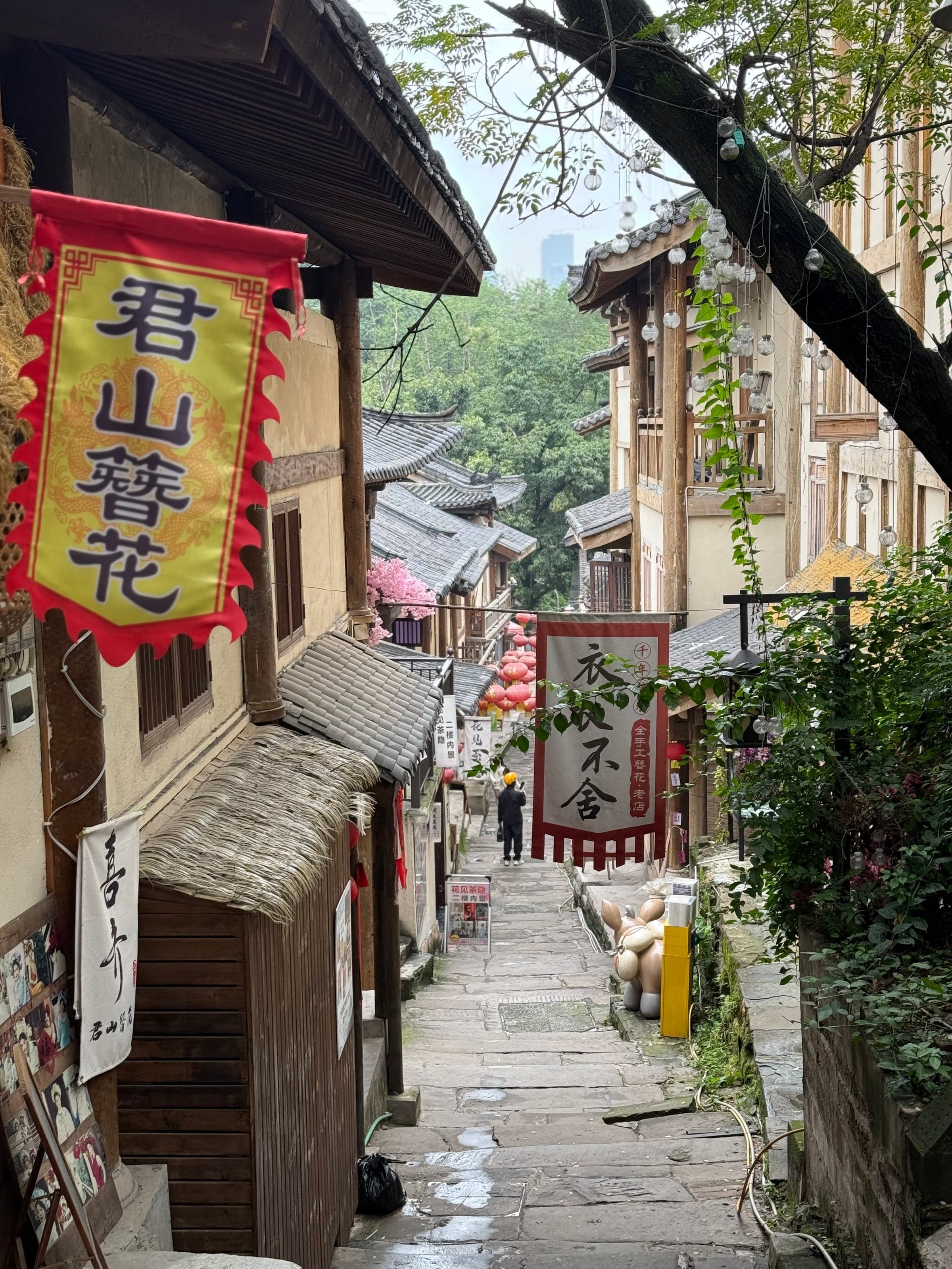 Ruelle en escaliers du vieux bourg de Ciqikou à Chongqing, bordée de boutiques aux bannières calligraphiées, passant descendant les marches pavées, téléphone à la main