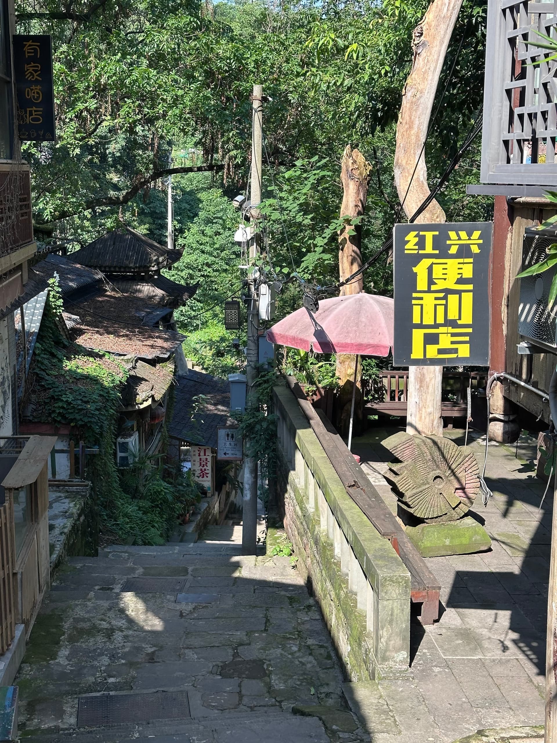 Enseigne jaune et noire d'un restaurant dans une ruelle végétalisée de Chongqing