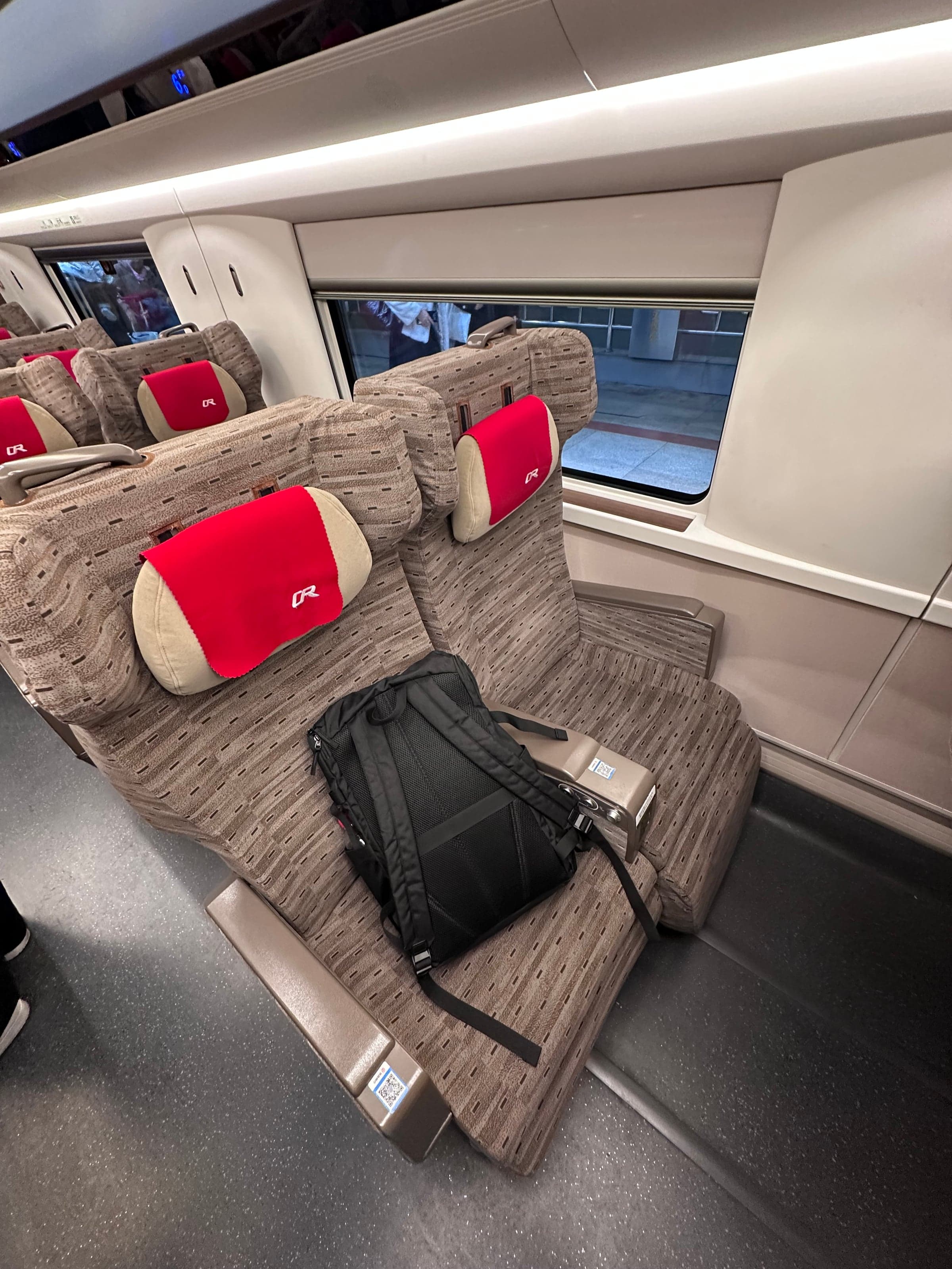 Rangée de sièges de seconde classe d'un TGV chinois, appuie-têtes rouges et tablette pliante, sac posé sur la banquette