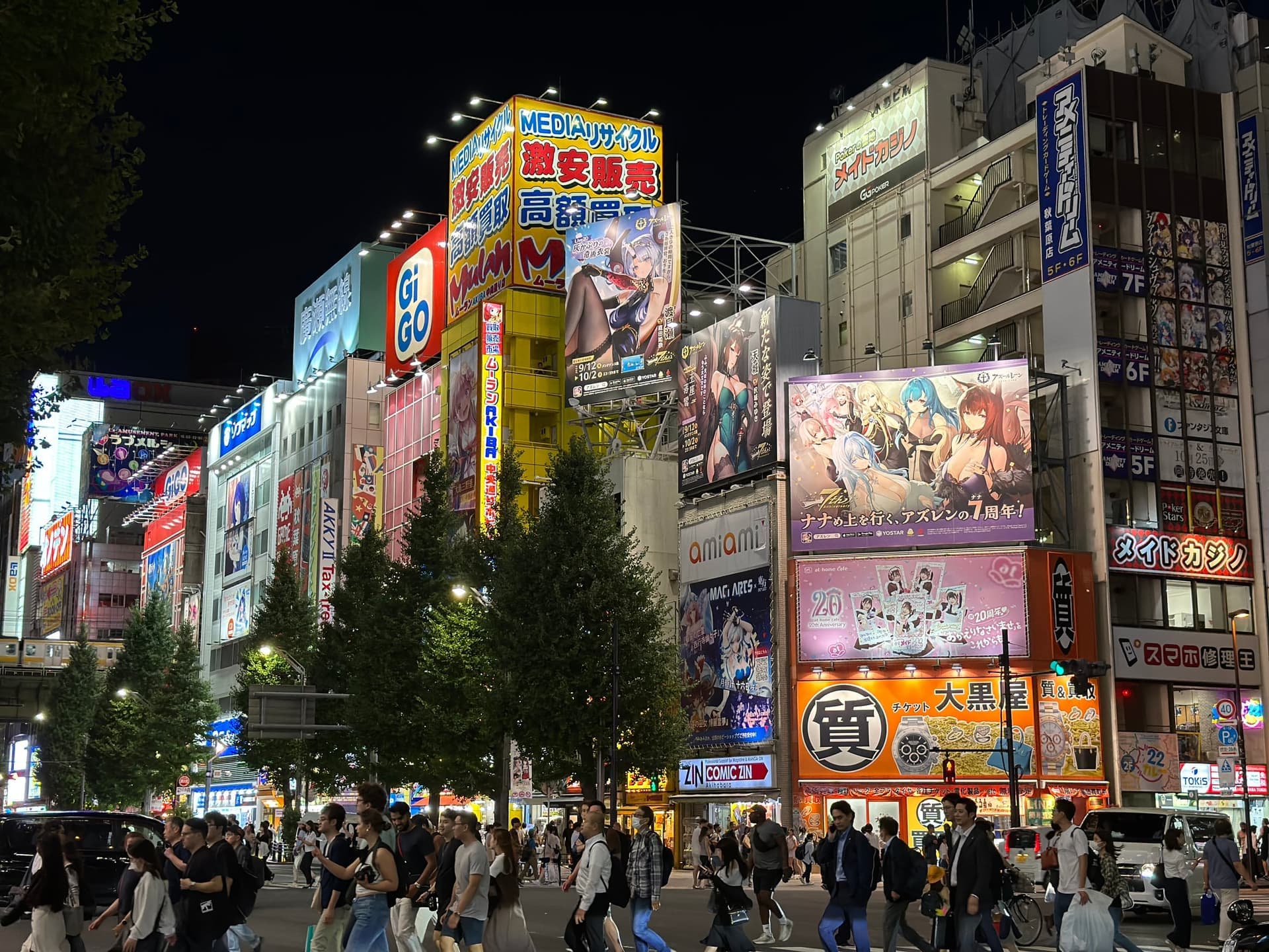 Carrefour d'Akihabara à Tokyo de nuit, façades couvertes d'enseignes lumineuses et d'affiches d'anime, foule traversant la rue