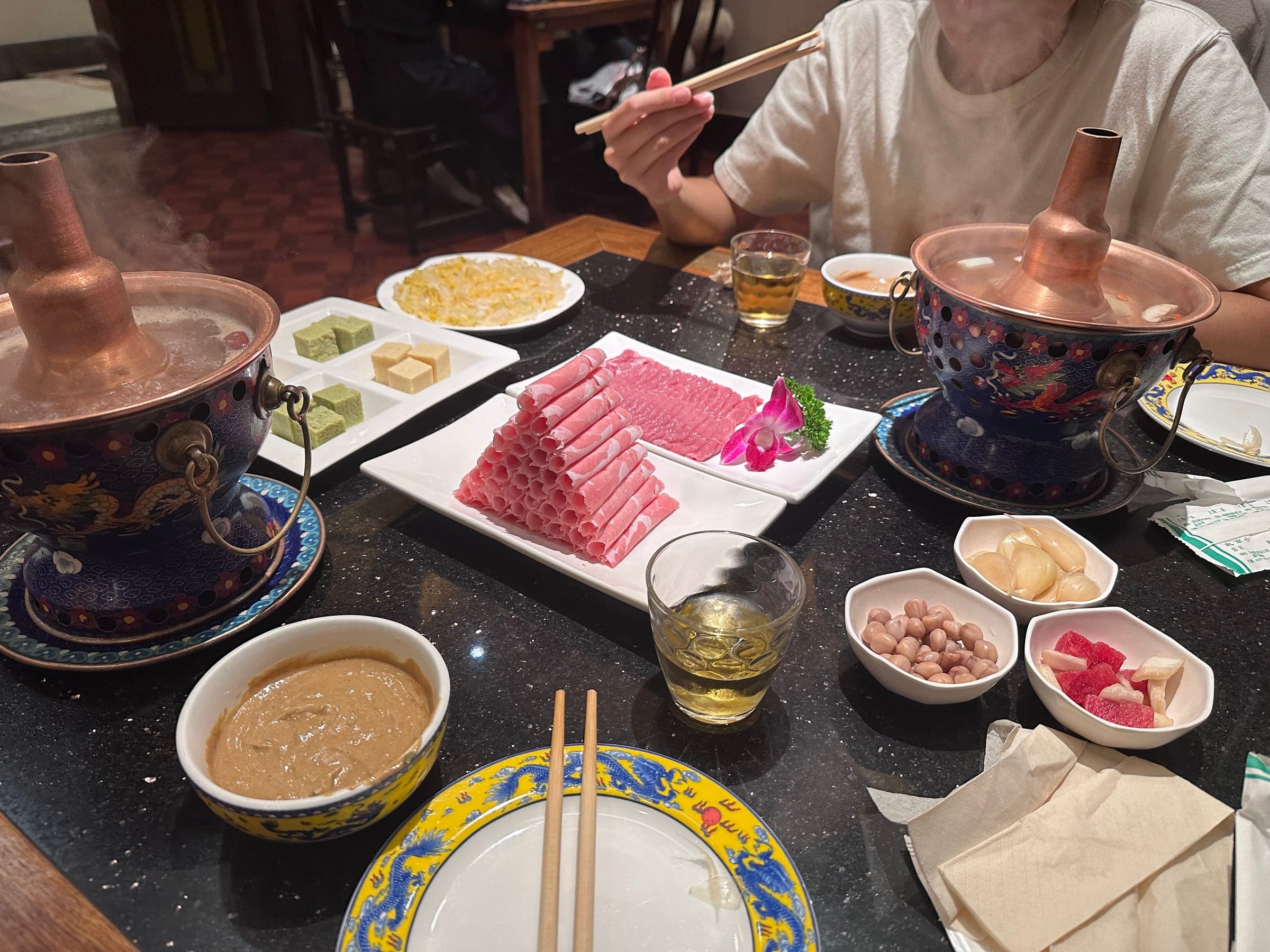 Hotpot pékinois au mouton dans des marmites en cuivre, fines tranches de mouton roulées et sauce au sésame