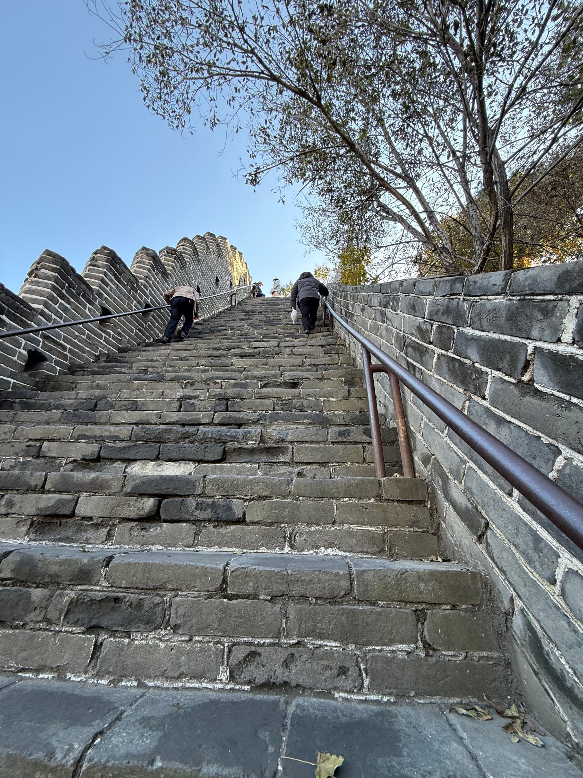 Escalier très pentu de la Grande Muraille à Badaling vu d'en bas, marches de pierre inégales, visiteurs agrippés à la rampe métallique