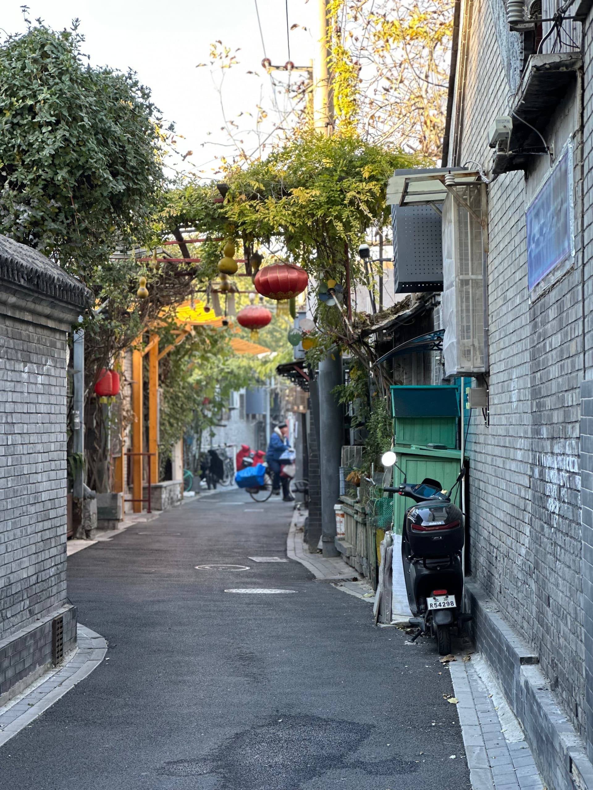 Ruelle traditionnelle des hutongs de Pékin, portes en bois rouge ornées, murs gris, vie quotidienne, lumière dorée du matin