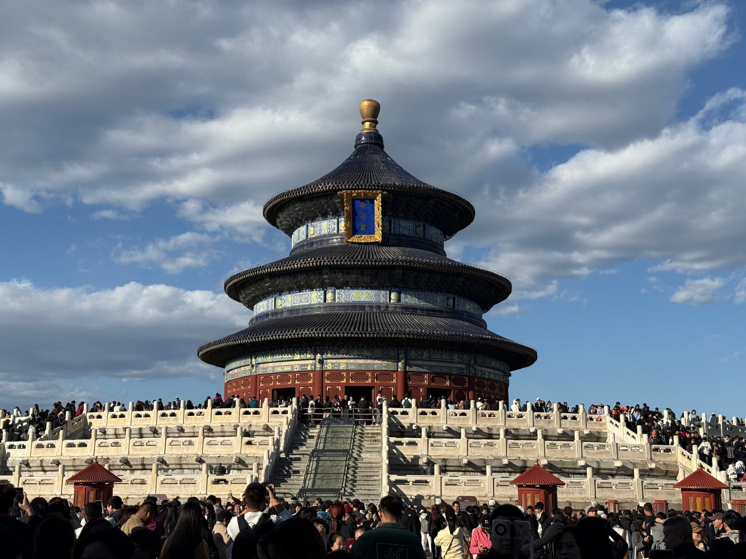 La salle des Prières pour de bonnes récoltes au Temple du Ciel de Pékin, rotonde à triple toiture de tuiles bleues surmontée d'un épi doré, posée sur une terrasse de marbre à trois étages, avec une foule dense de visiteurs au pied et sur les balustrades
