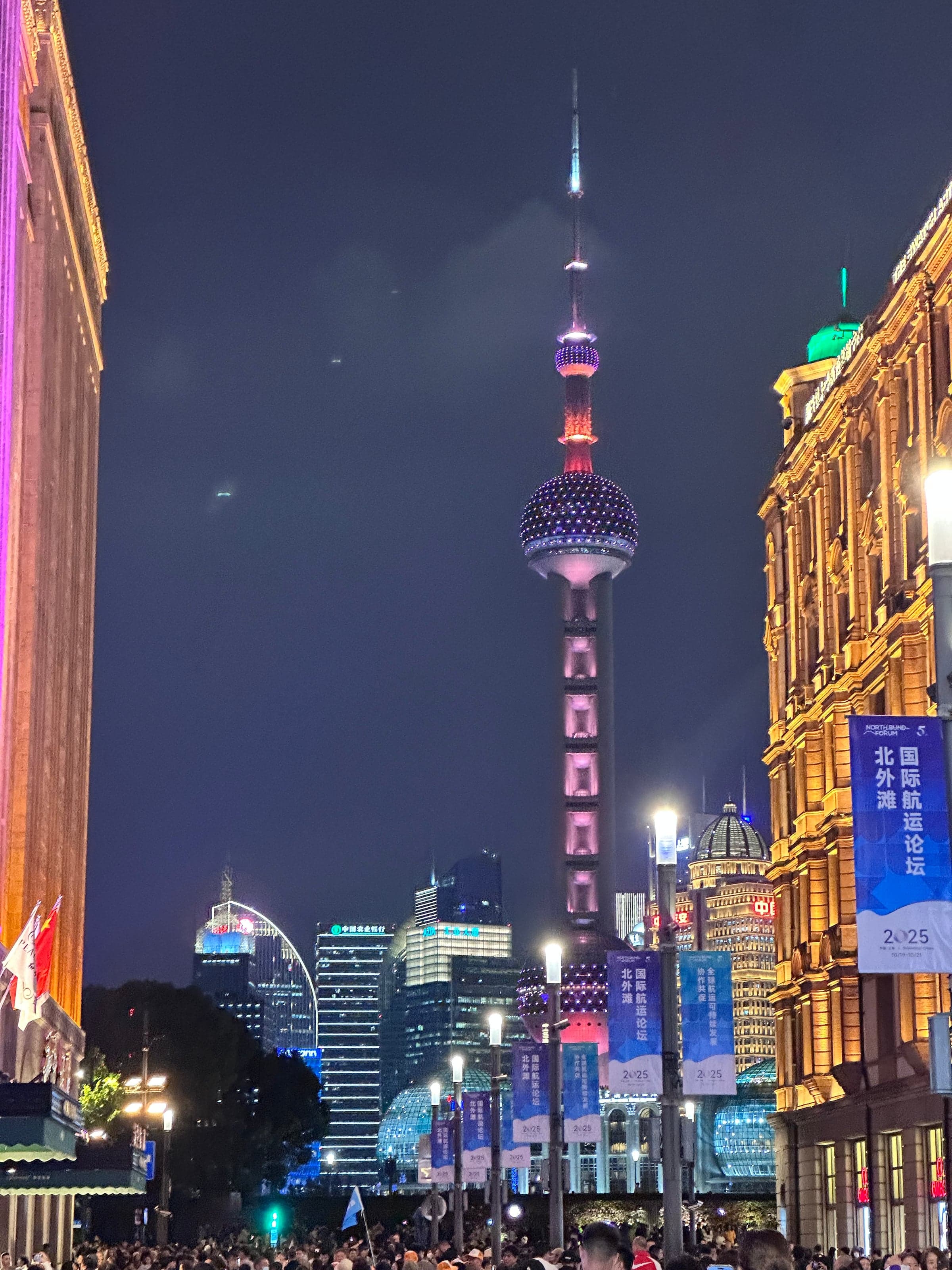 Tour Perle de l'Orient illuminée en rose vue depuis la rue de Nankin, façade historique éclairée à droite, foule dense et enseignes lumineuses en contrebas