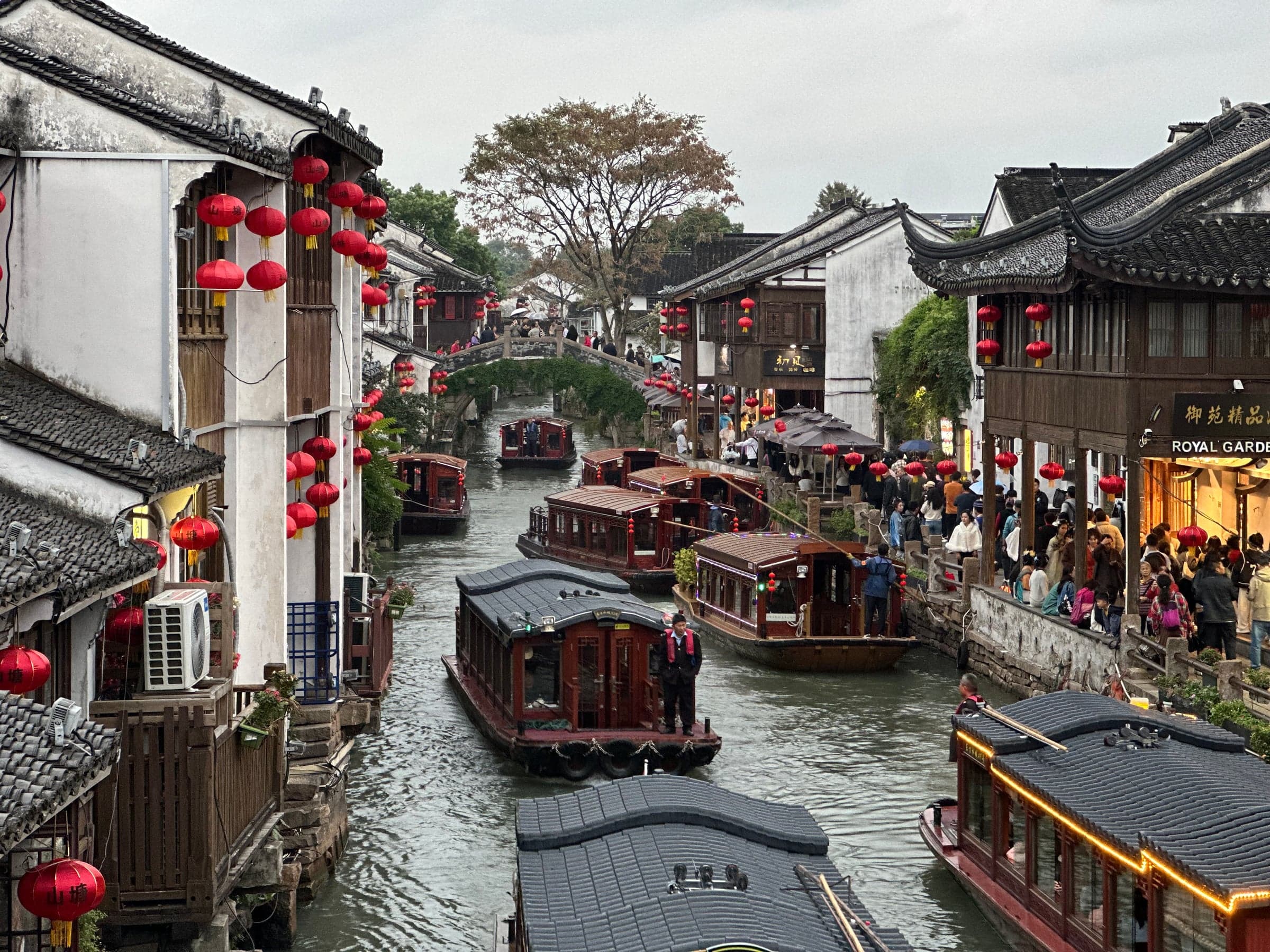 Canal Shantang à Suzhou en journée, barques de bois couvertes circulant entre les maisons anciennes, lanternes rouges accrochées aux façades et promeneurs sur les quais