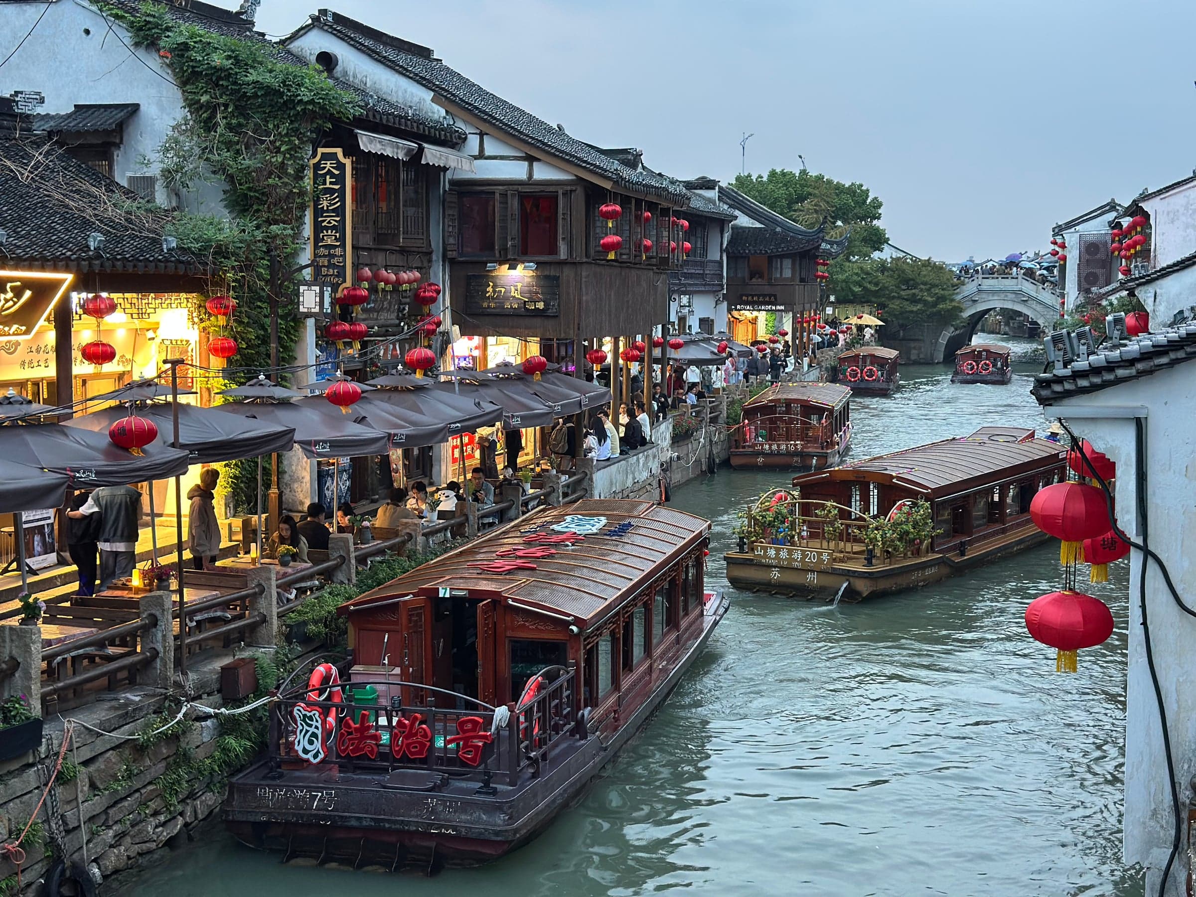 Canal Shantang à Suzhou au crépuscule, bateaux traditionnels en bois, maisons blanches aux toits gris, lanternes rouges et pont en dos d'âne au fond