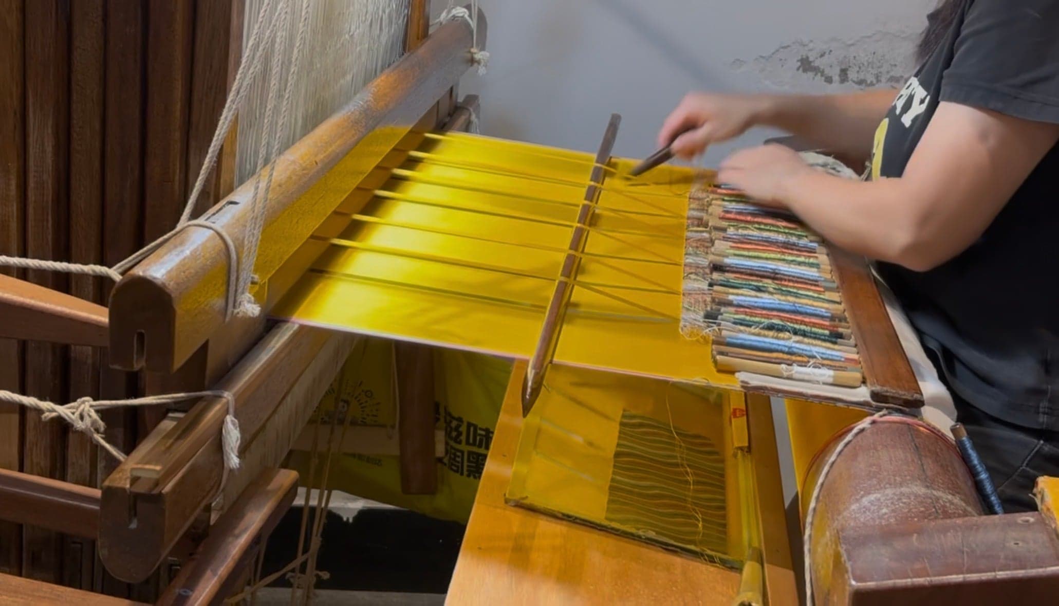 Tissage de la soie sur un métier à bras traditionnel à Suzhou, soie jaune tendue entre les lisses, navette de bois et bobines de fil de couleur
