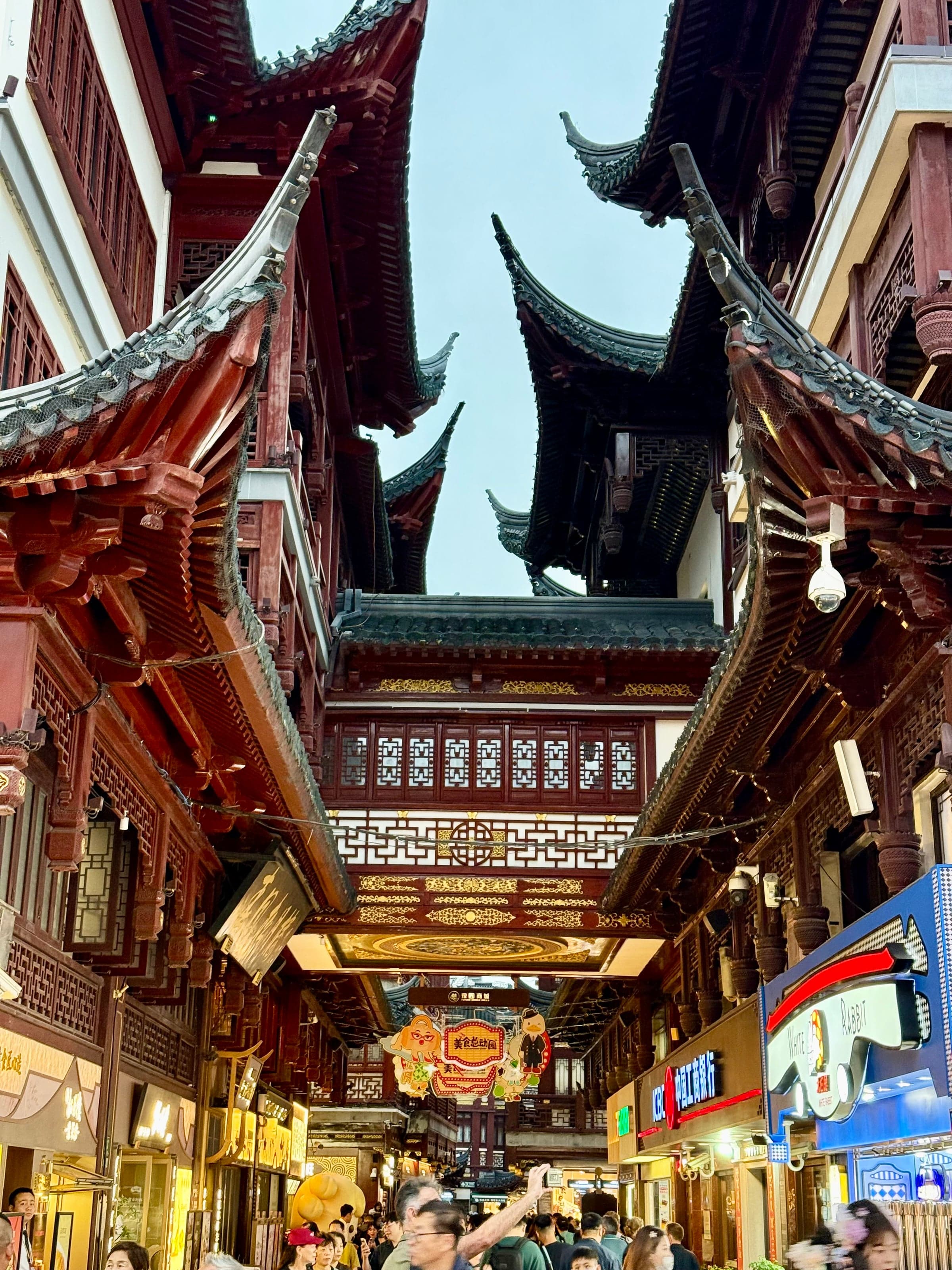 Ruelle du bazar de Yuyuan à Shanghai à la tombée du jour : toits traditionnels aux avant-toits relevés, enseignes lumineuses de boutiques modernes au rez-de-chaussée et foule dense