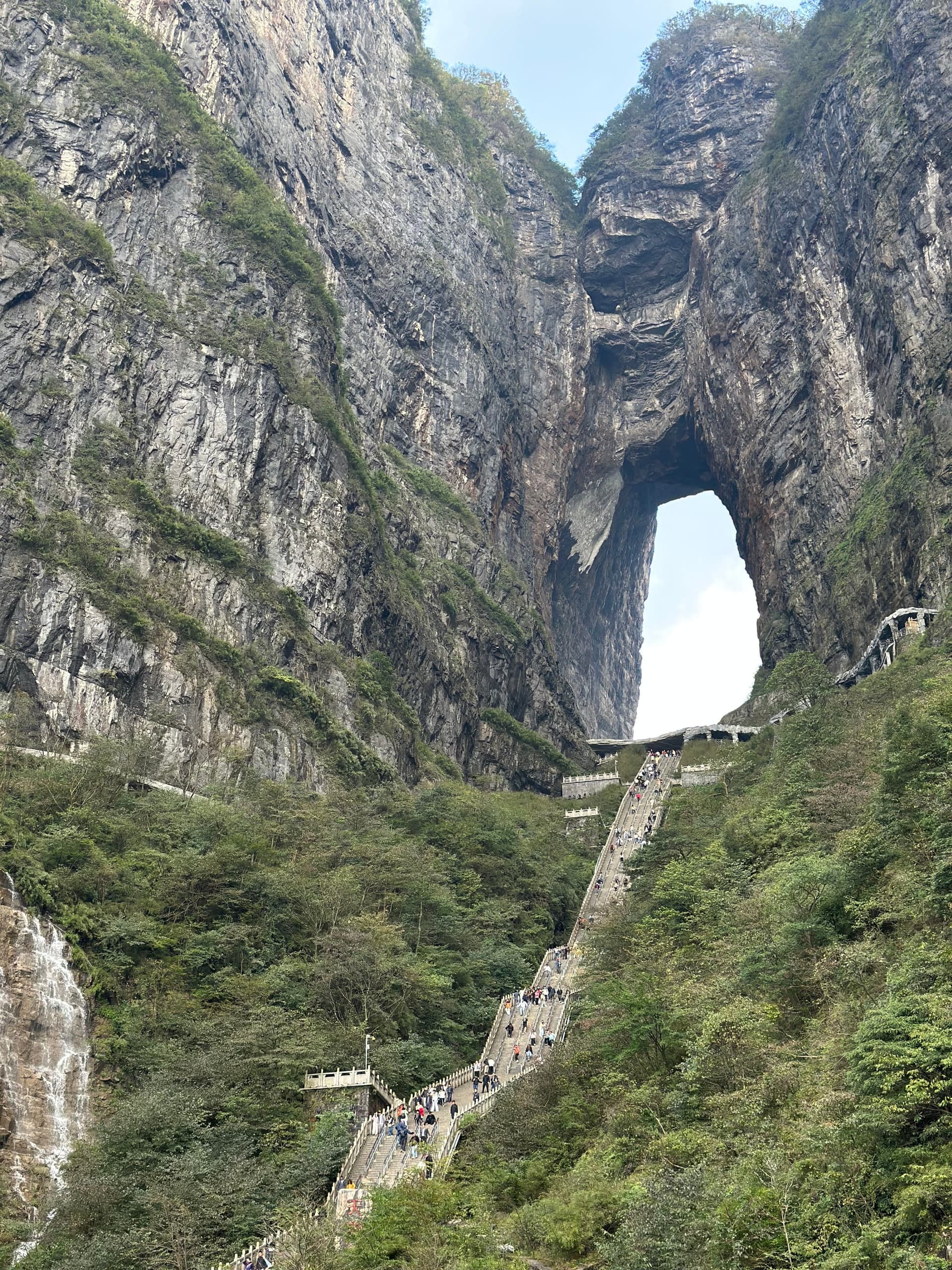 Arche naturelle percée dans une haute falaise de la montagne Tianmen, avec l'escalier de 999 marches montant en zigzag jusqu'à l'ouverture et des visiteurs réduits à des points