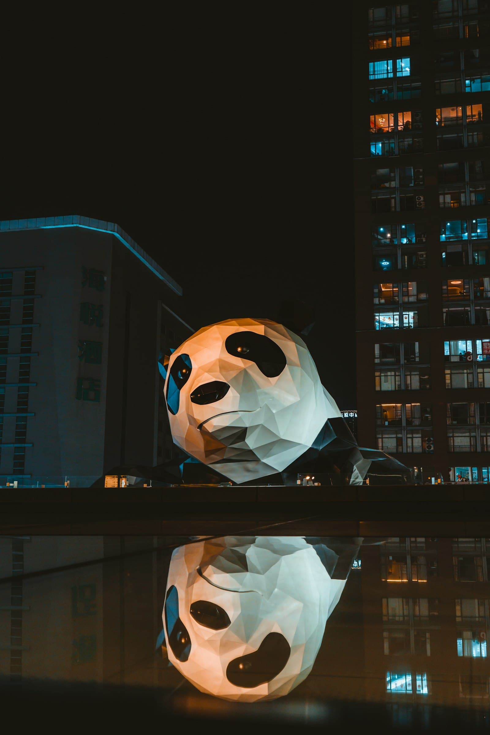 Sculpture lumineuse de panda géant escaladant un bâtiment au centre IFS de Chengdu, la nuit, reflétée dans l'eau