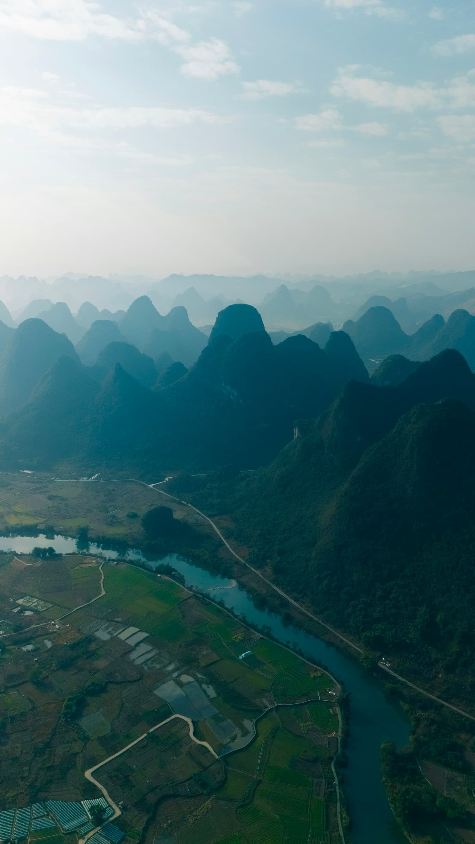 Vue aérienne de la campagne de Yangshuo, des pics karstiques en enfilade dans la brume au-dessus d'une rivière qui serpente entre les rizières et les villages