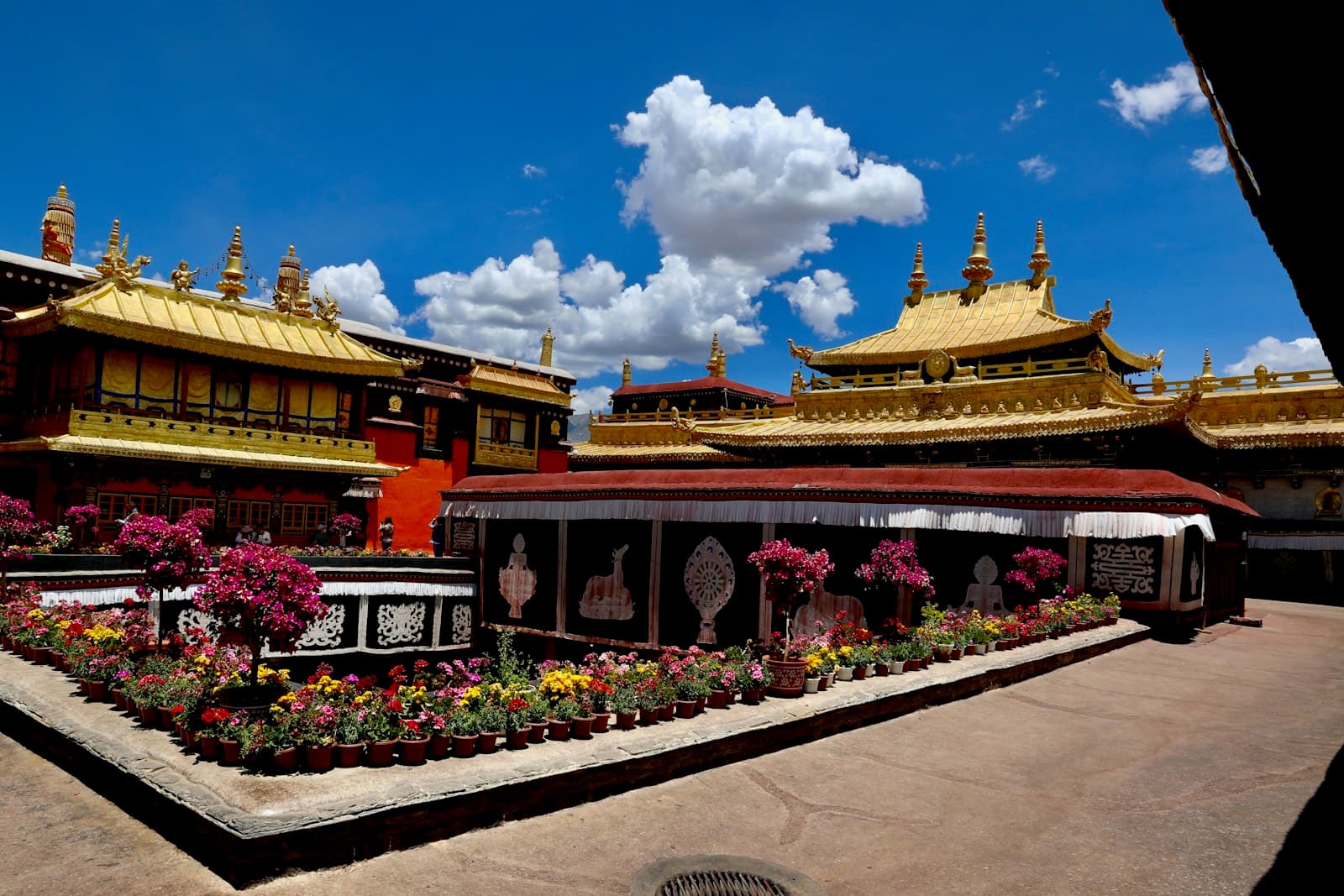 Les toits dorés du temple du Jokhang à Lhassa sous un ciel bleu, bâtiments rouges et blancs bordés de pots de fleurs dans la cour intérieure