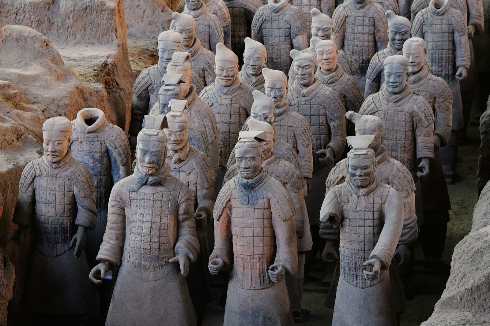 Rangs de guerriers en terre cuite alignés dans une tranchée de fouille de la fosse 1 à Xi'an, visages tous différents, armures à écailles rivetées dont l'une conserve des traces de pigment rouge, parois de terre ocre de part et d'autre