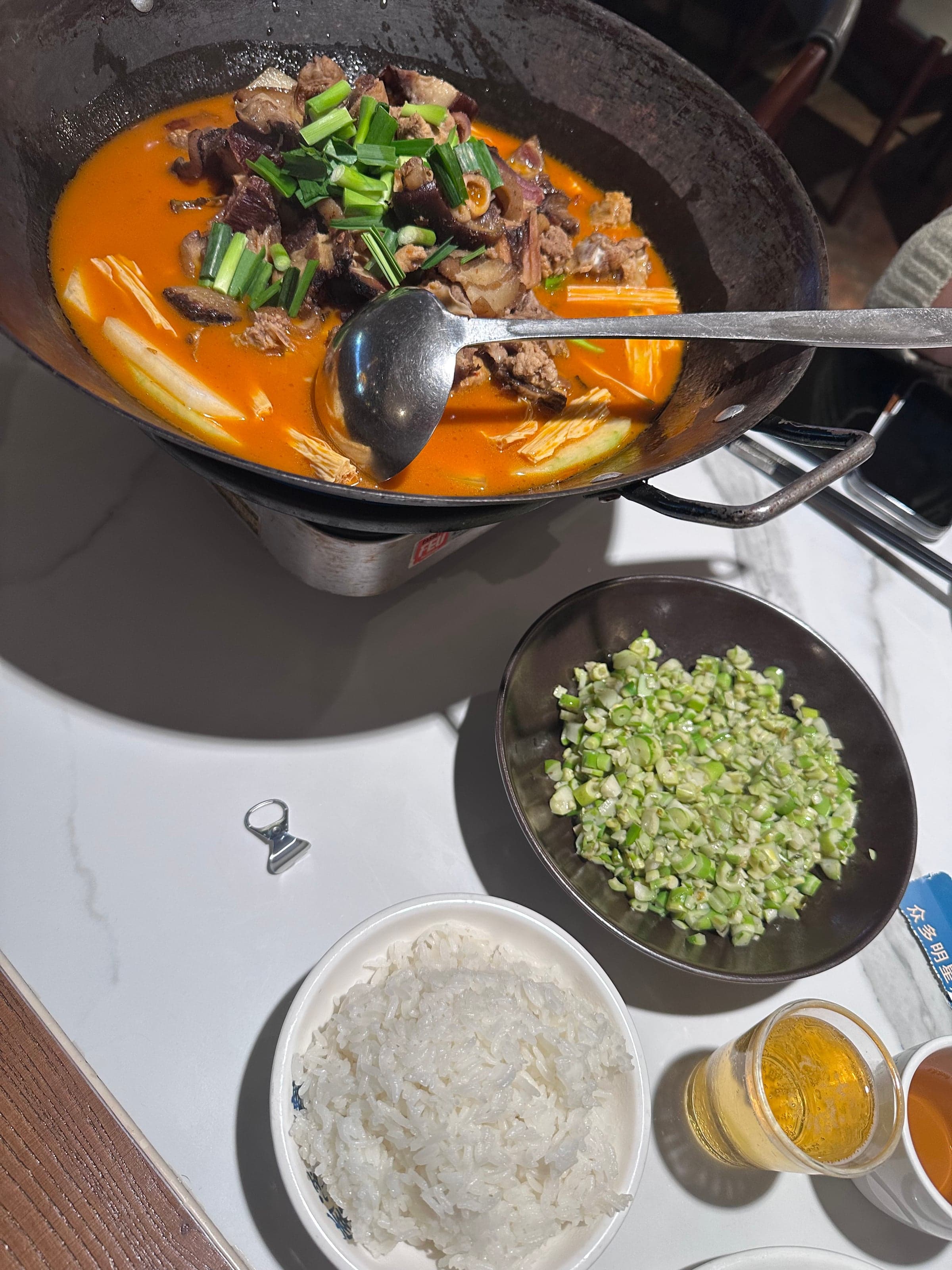 Plat braisé épicé servi sur un réchaud : morceaux de viande mijotés dans une sauce rouge à l'huile pimentée et ciboule, avec un bol de riz à côté