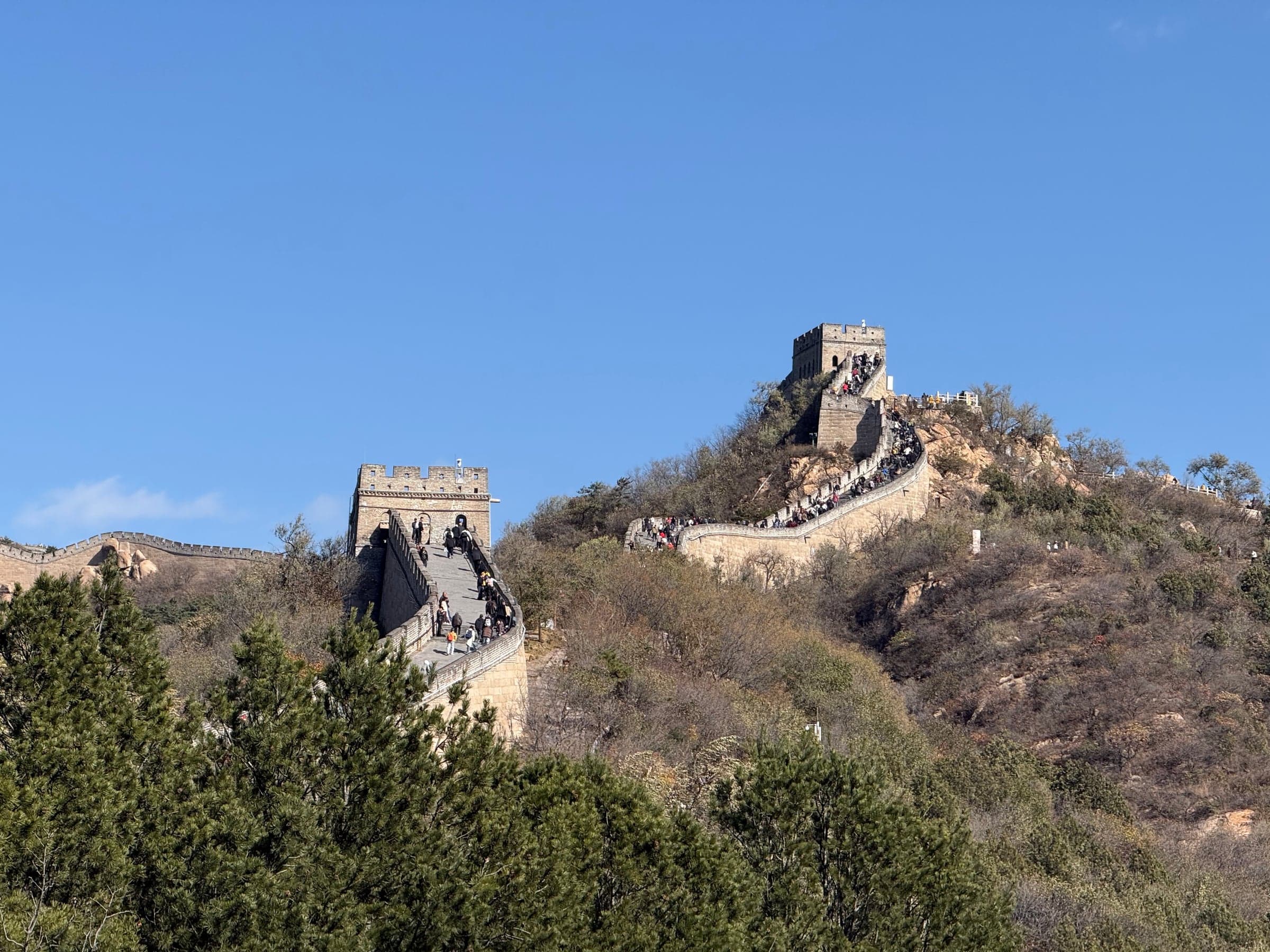La Grande Muraille à Badaling sous un ciel bleu : le rempart et ses tours de guet suivent la ligne des crêtes, files de visiteurs sur les rampes