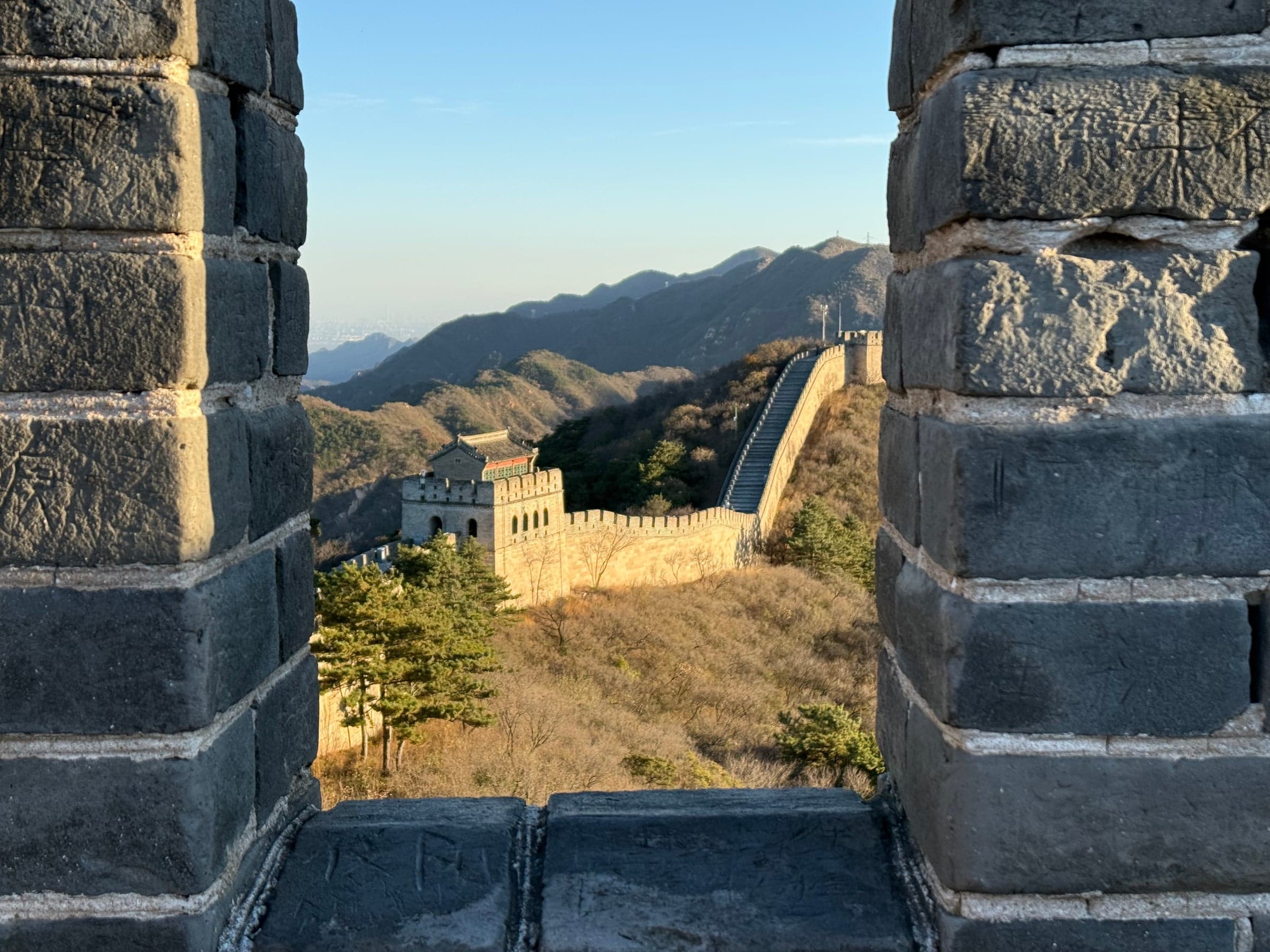 La Grande Muraille et une tour de guet vues à travers l'ouverture en pierre d'une tour à Badaling, lumière chaude de fin de journée