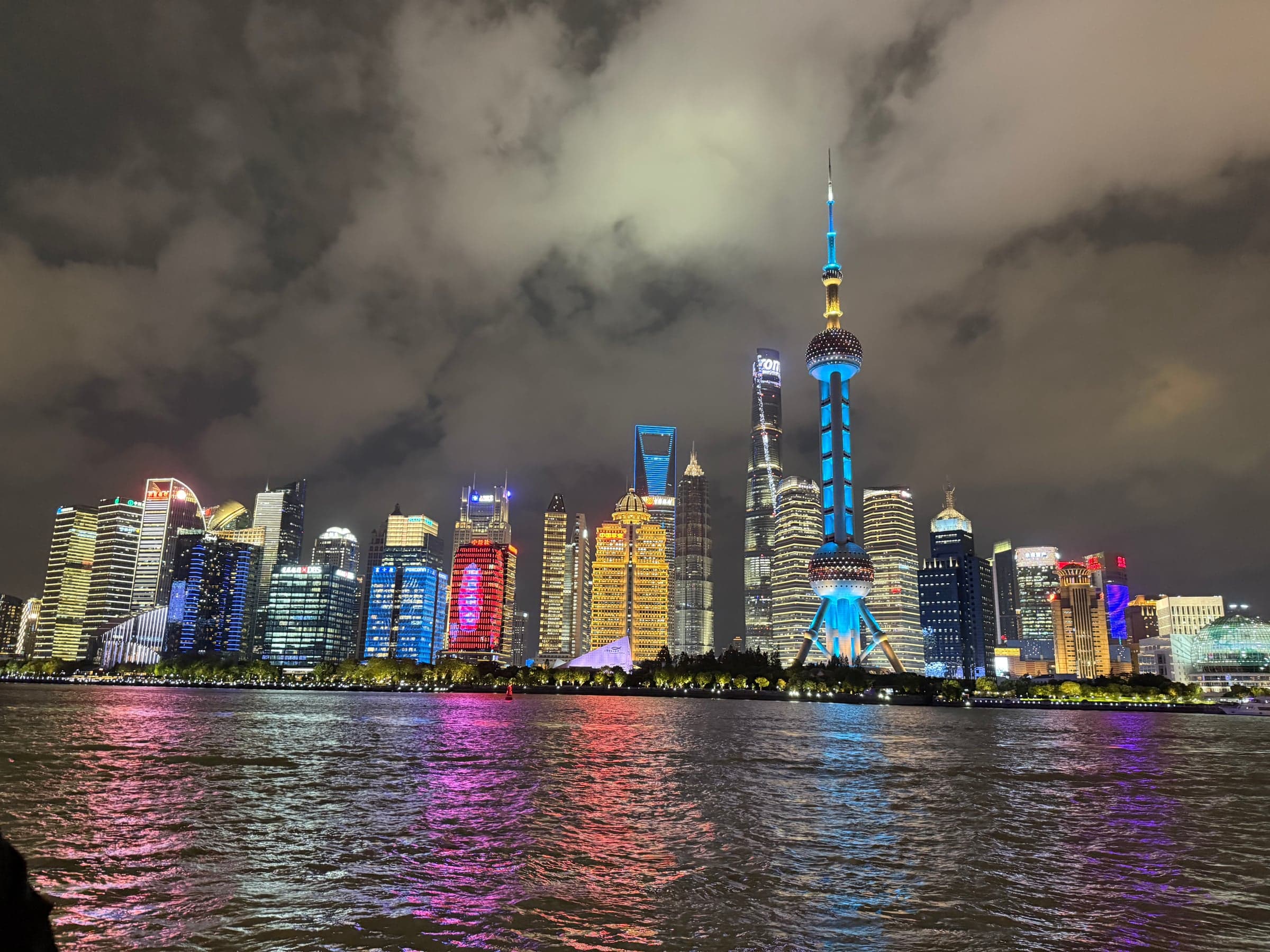 Skyline illuminée de Pudong à Shanghai la nuit vue depuis le Bund, tour Perle de l'Orient en bleu, gratte-ciel aux façades LED et reflets colorés sur le fleuve Huangpu