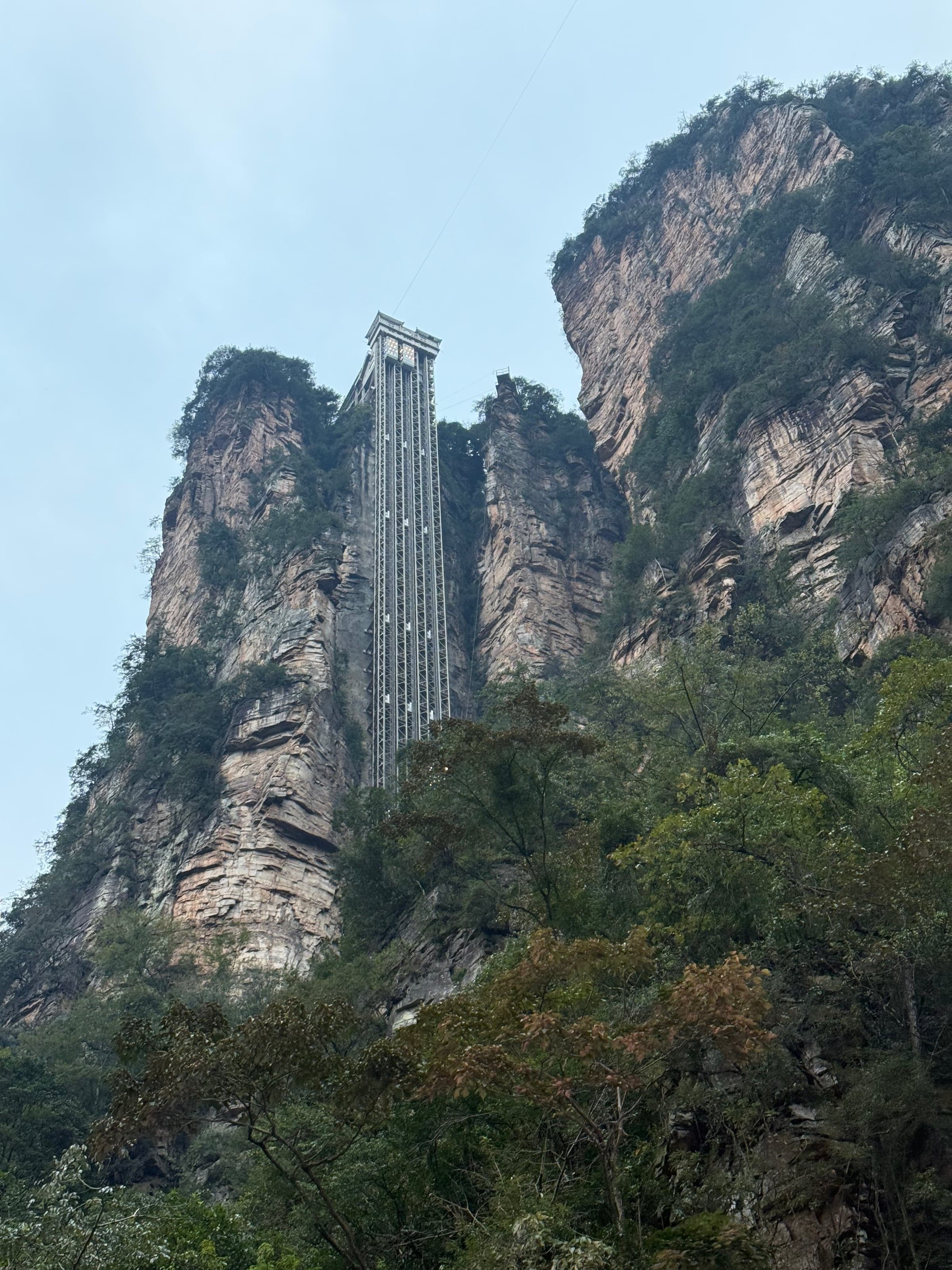 Ascenseur de verre Bailong plaqué contre une falaise de grès verticale, vu depuis le bas