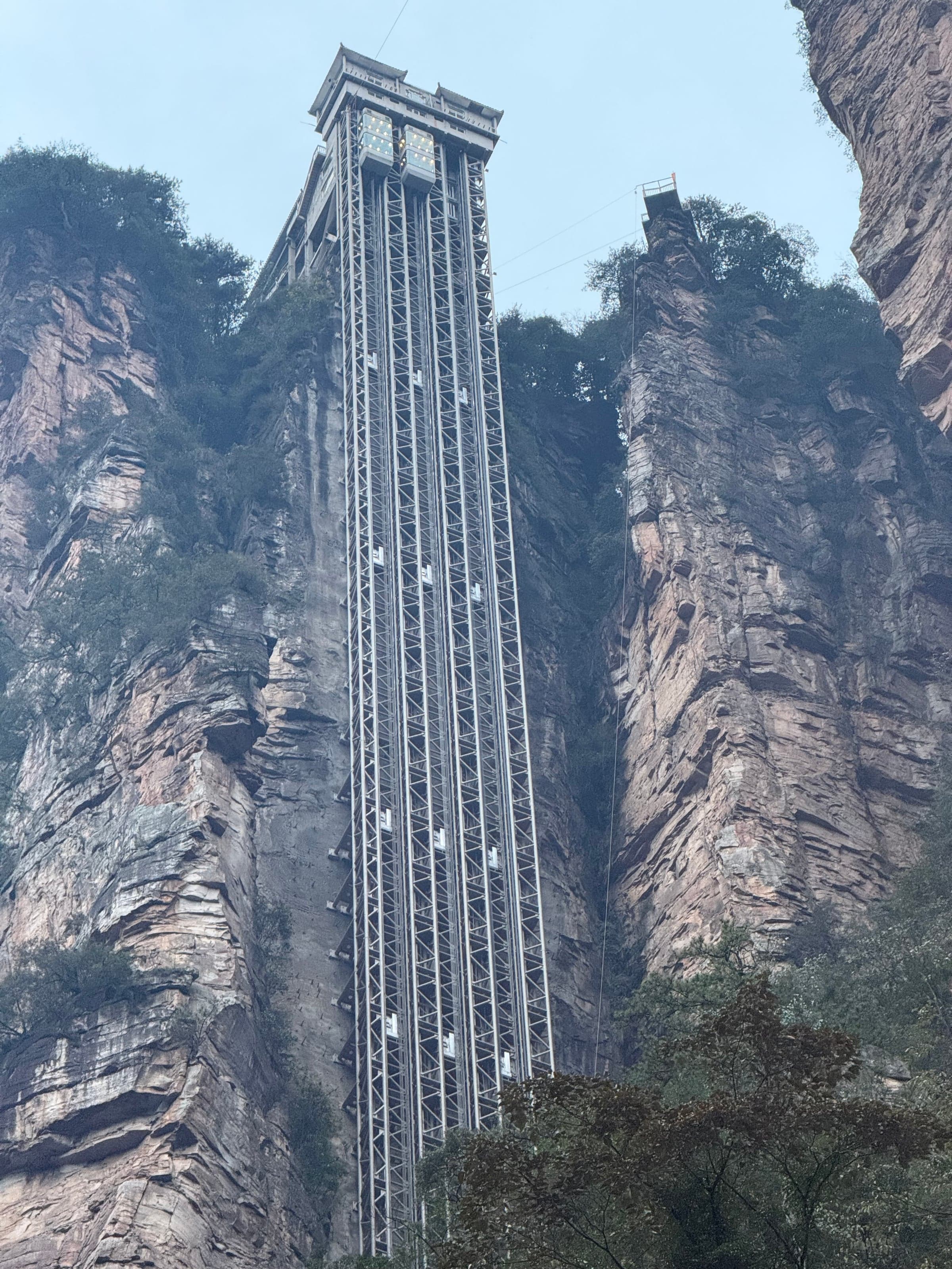Structure métallique de l'ascenseur Bailong dressée contre une falaise de grès, cabines vitrées visibles le long du rail, piliers rocheux de part et d'autre