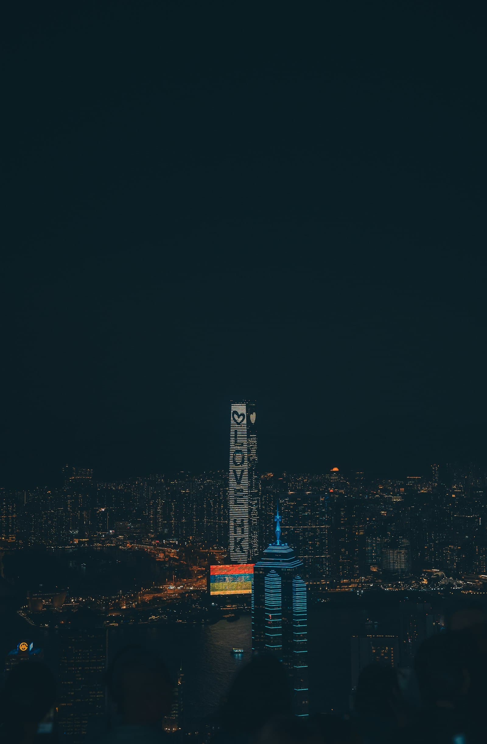 Gratte-ciel illuminés de Hong Kong la nuit vus depuis les hauteurs, tours serrées descendant vers le port de Victoria