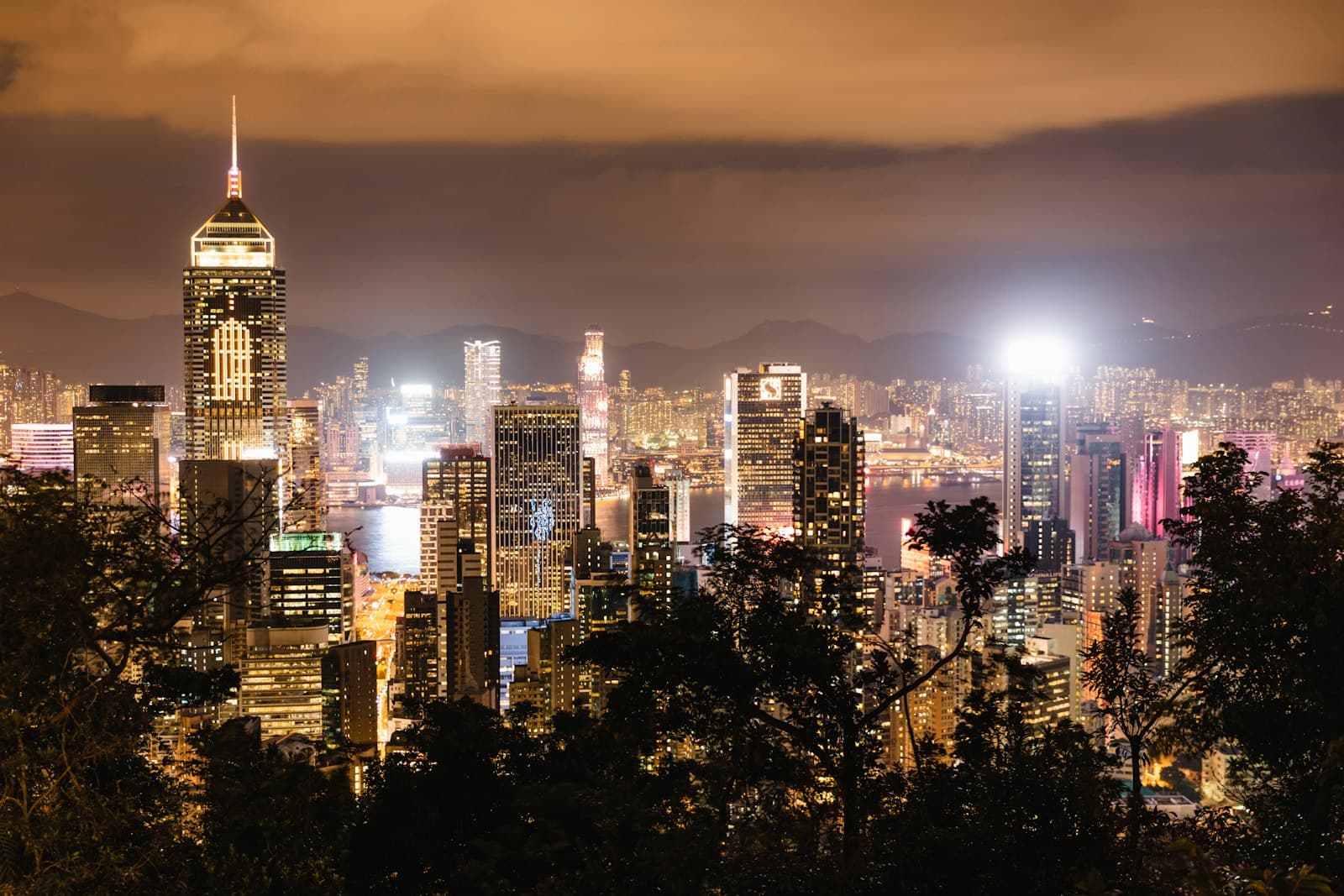 Skyline illuminée de Hong Kong vue depuis les hauteurs de Victoria Peak la nuit, gratte-ciel éclairés autour du port de Victoria et collines de Kowloon en arrière-plan
