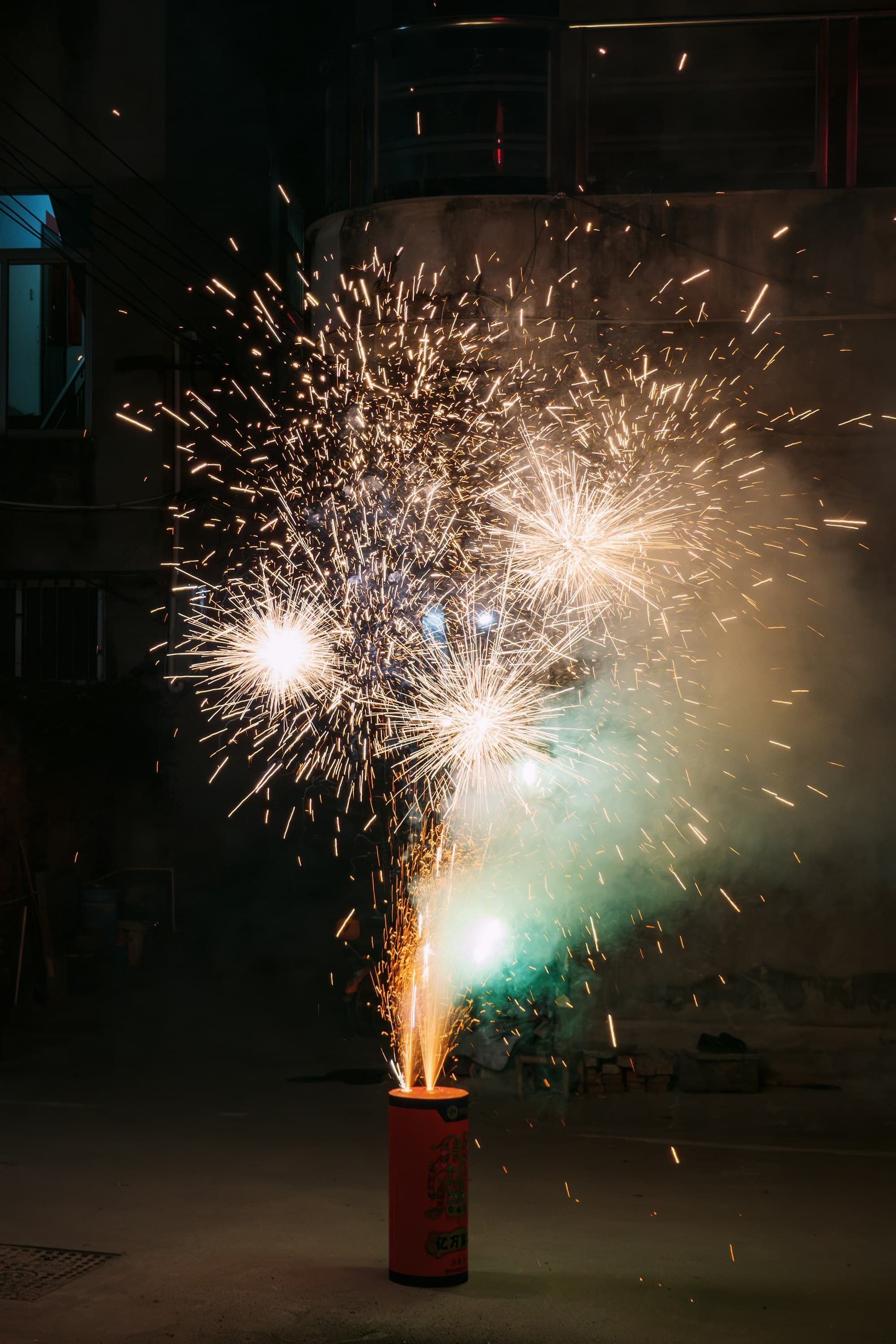 Feu d'artifice de sol crachant des gerbes d'étincelles dans une cour résidentielle chinoise, la nuit