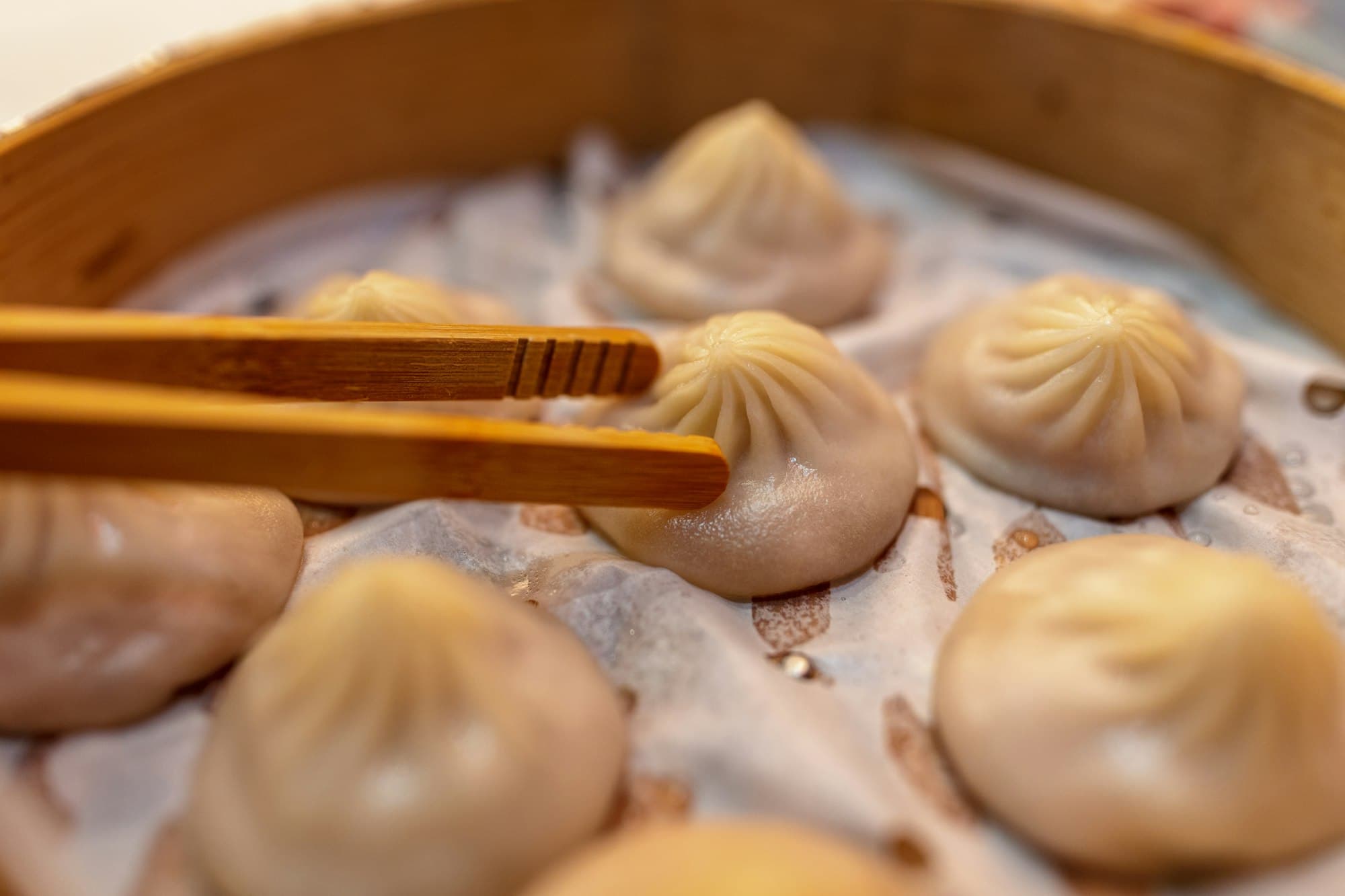 Raviolis chinois à la vapeur dans un panier de bambou, saisis avec des baguettes
