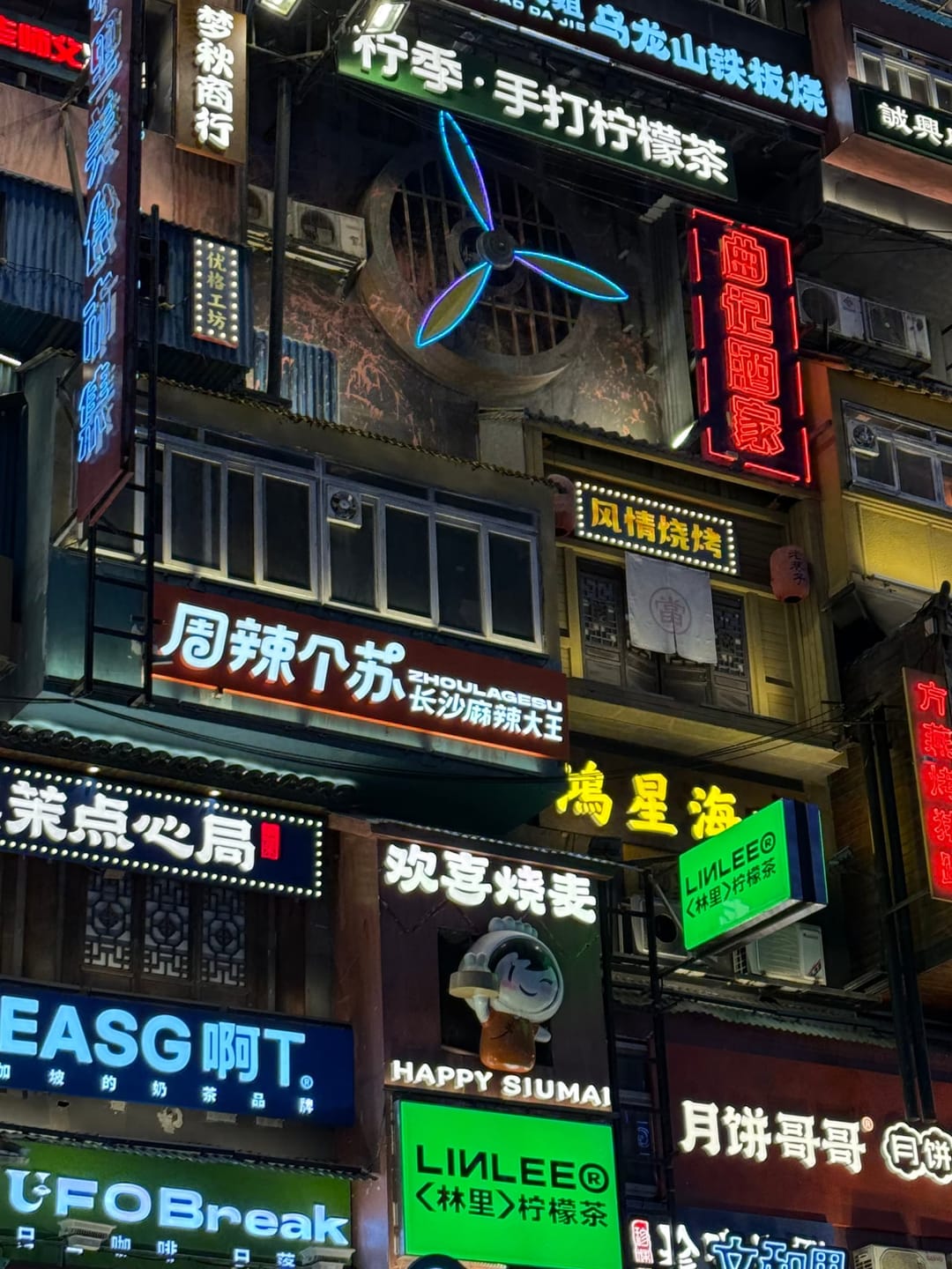 Rue de nuit à Changsha saturée d'enseignes au néon en caractères chinois, dont une échoppe de cuisine pimentée et une chaîne de thé au citron