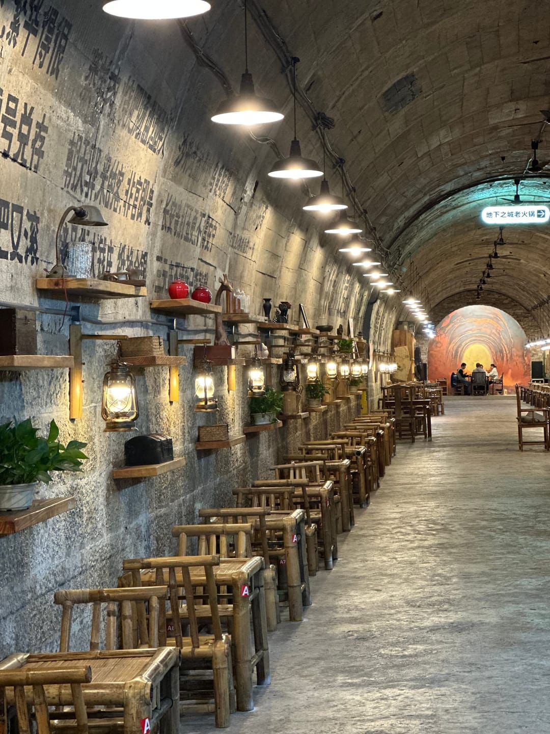 Intérieur d'un tunnel anti-aérien converti en restaurant de hotpot, avec braseros encastrés et tabourets en bambou