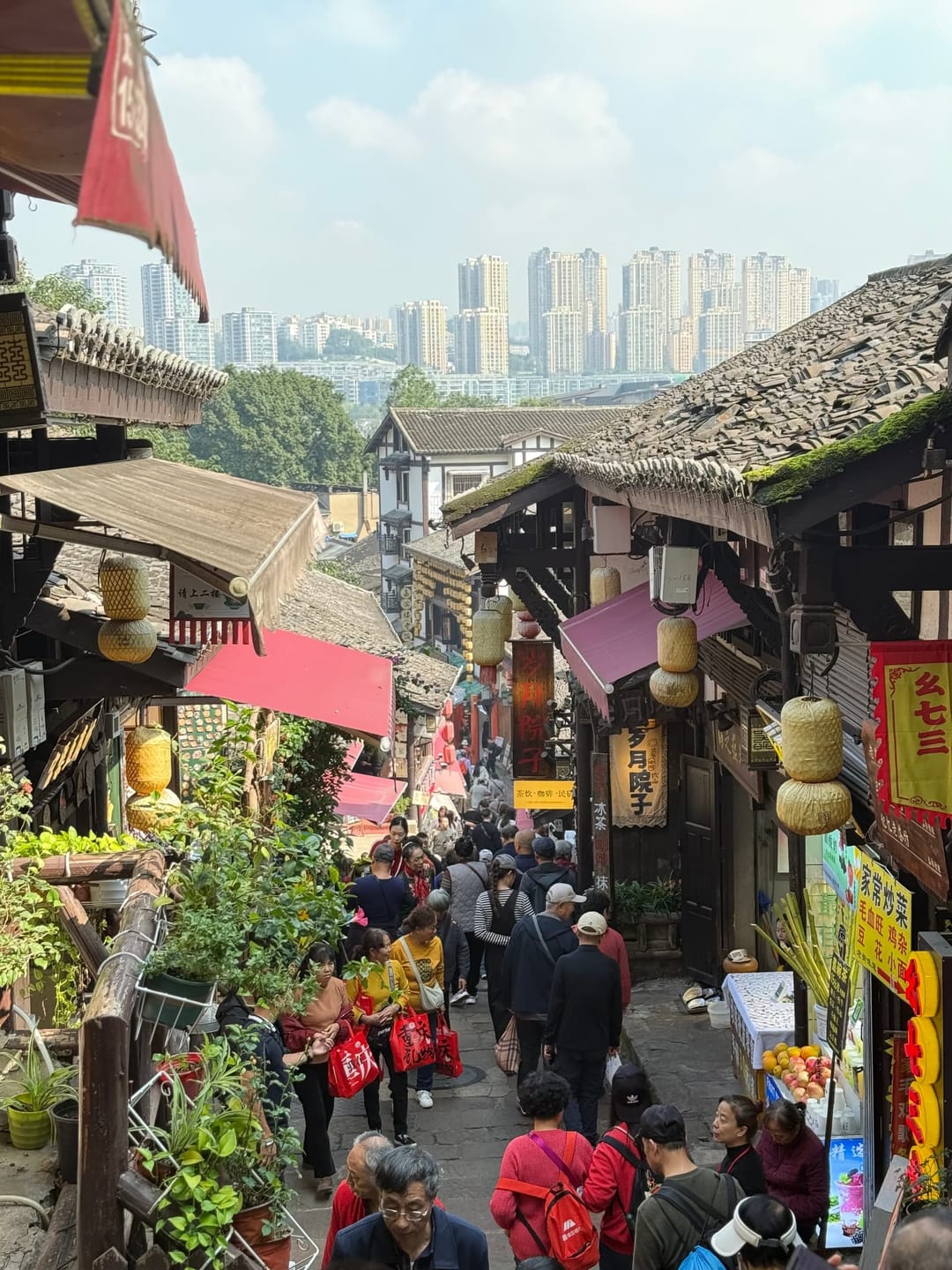 Vue en hauteur sur le bourg de Ciqikou, ses toits de tuiles noires, la foule et les immeubles modernes derrière