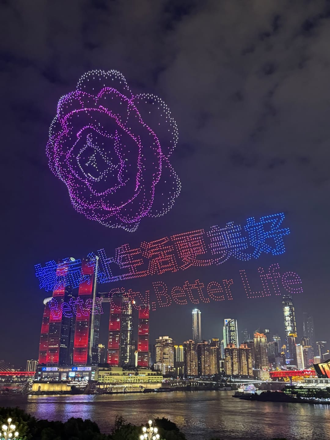 Formation de drones formant une rose lumineuse violette et un texte au-dessus de la skyline illuminée de Chongqing