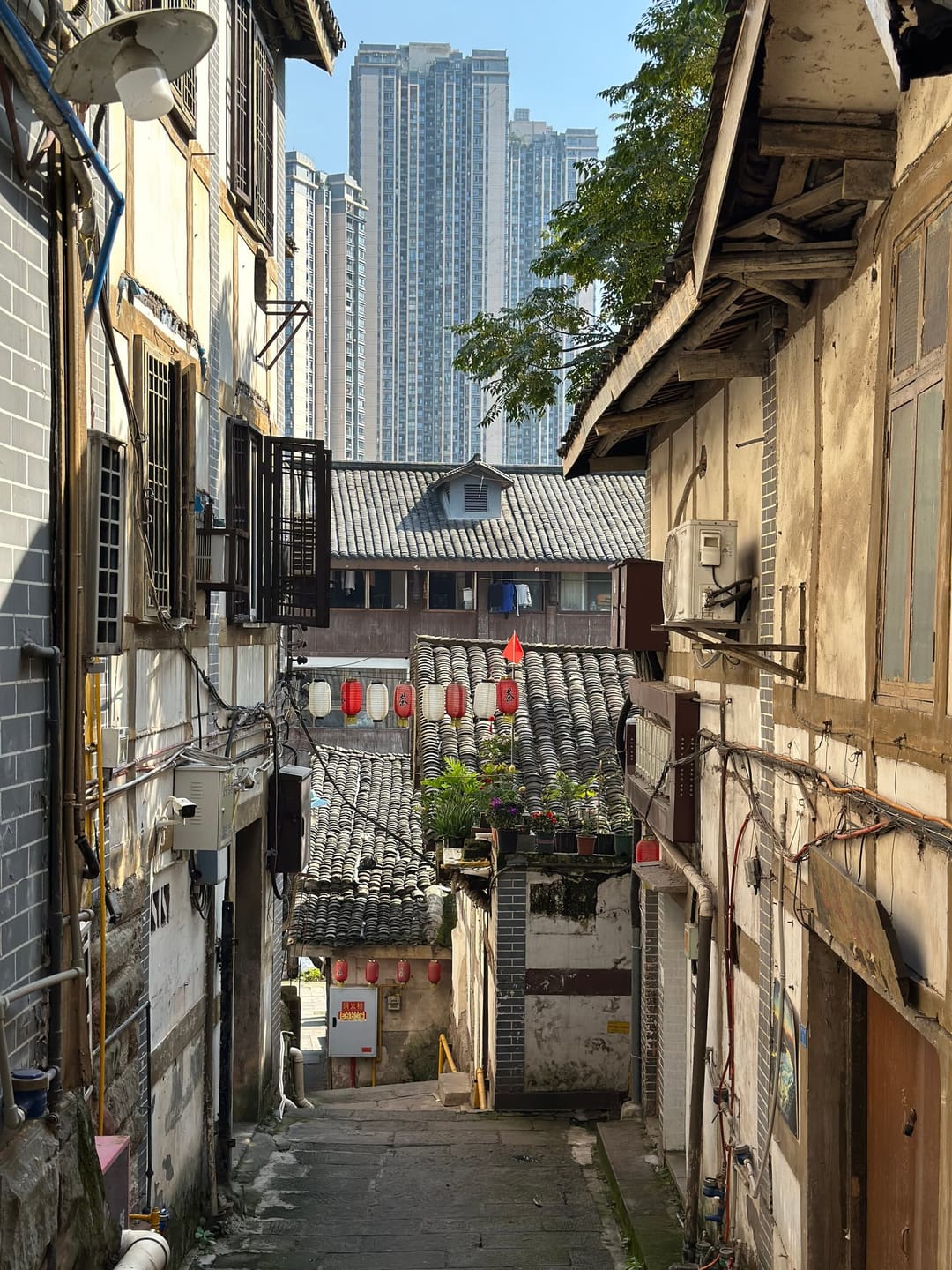 Maison ancienne avec fils électriques en contre-plongée, une tour de verre moderne se dressant immédiatement derrière