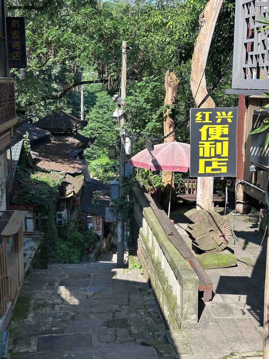 Enseigne jaune et noire d'un restaurant dans une ruelle végétalisée de Chongqing