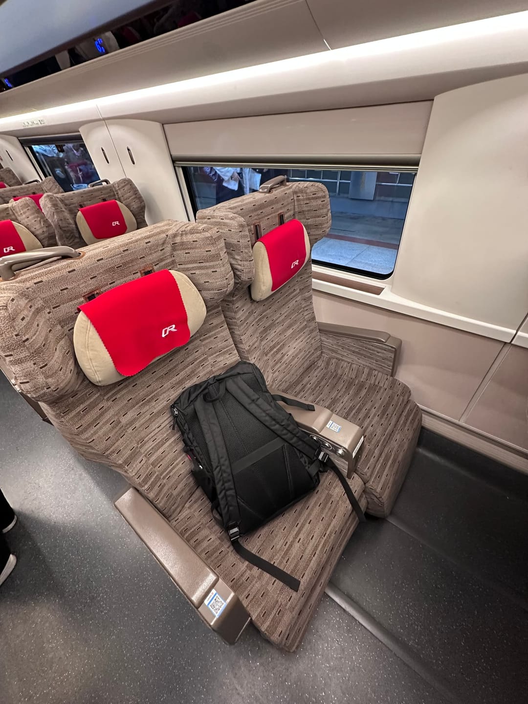Rangée de sièges de seconde classe d'un TGV chinois, appuie-têtes rouges et tablette pliante, sac posé sur la banquette