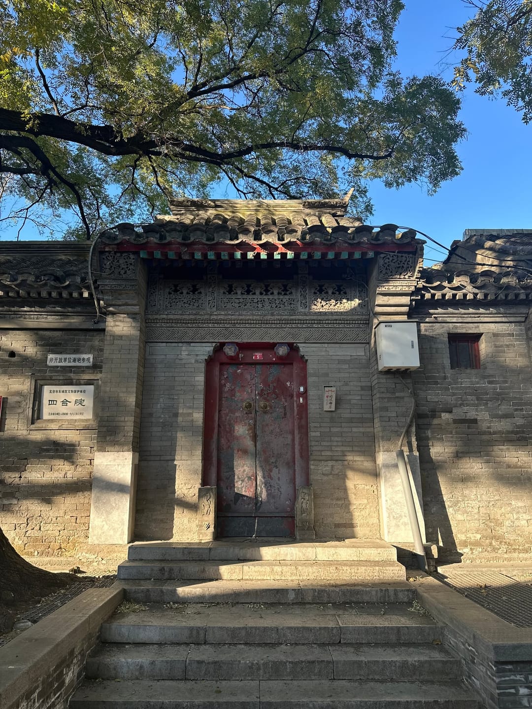 Portail de hutong à double vantail rouge sous des panneaux de briques finement sculptées, plaque blanche à caractères chinois signalant que le lieu n'est pas ouvert aux visiteurs