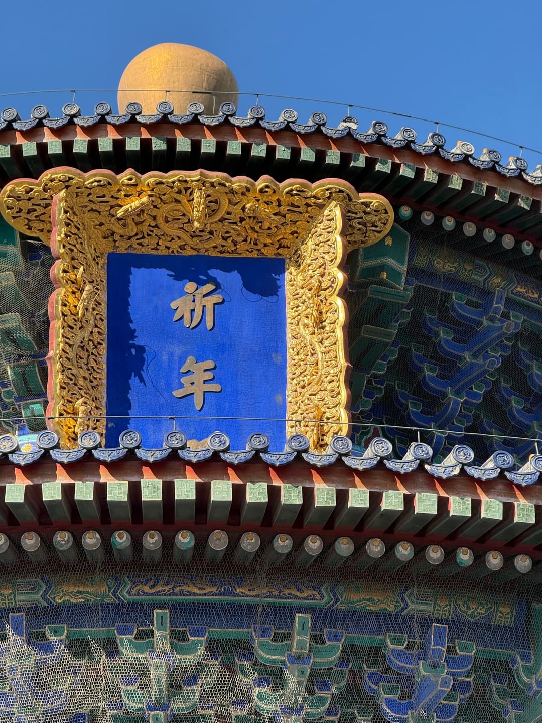 Gros plan sur la plaque bleue à caractères dorés de la salle des Prières, dans son encadrement doré, sertie sous des avant-toits peints de bleu, vert et rouge