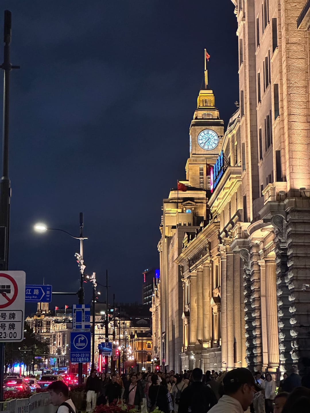 La tour de l'horloge de l'ancienne maison des douanes sur le Bund à Shanghai, illuminée la nuit, façades coloniales alignées et foule sur le trottoir
