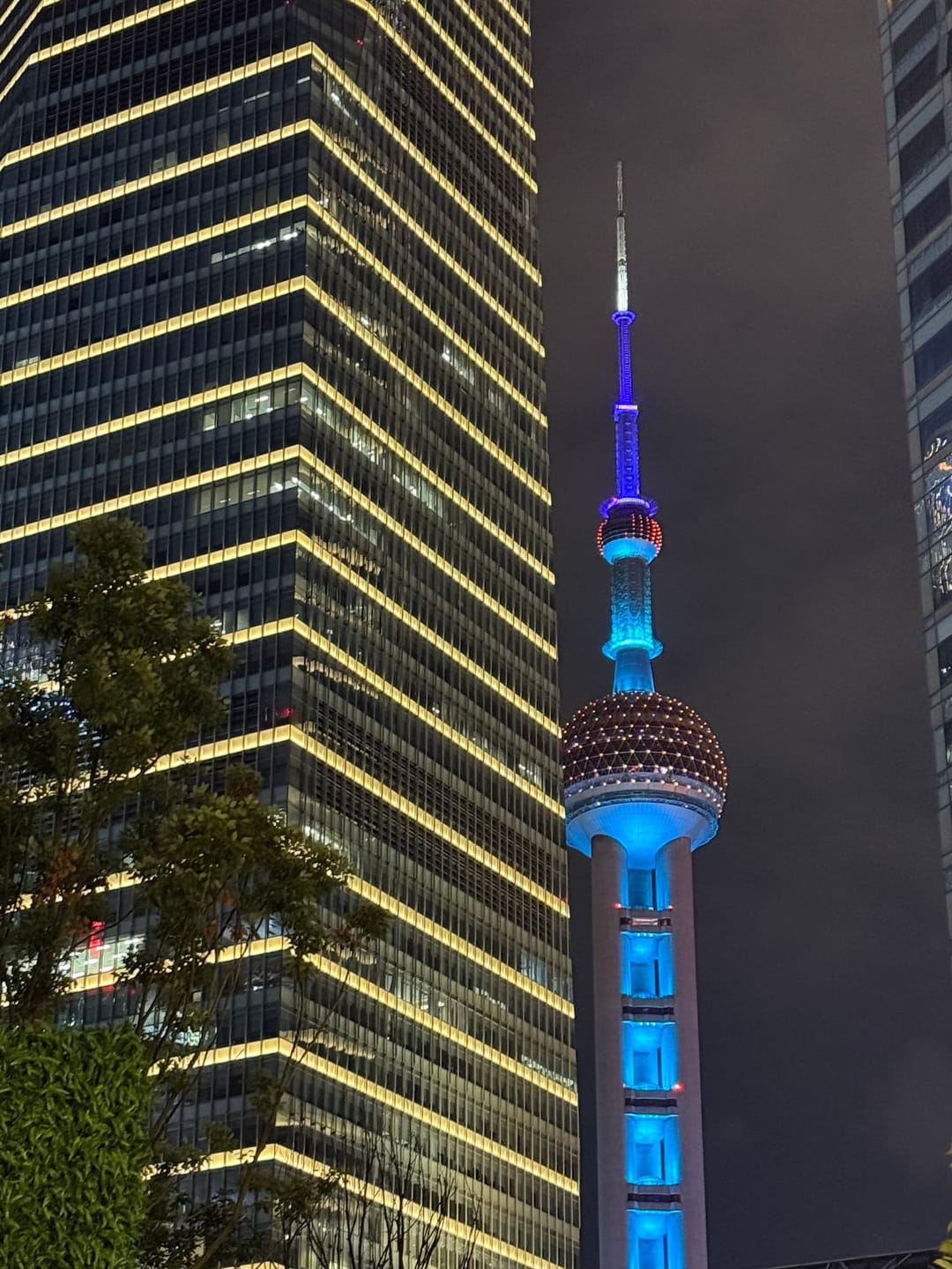 Perle de l'Orient illuminée en bleu et rouge la nuit à Shanghai, cadrage rapproché depuis le Bund, gratte-ciel doré du World Financial Center à gauche