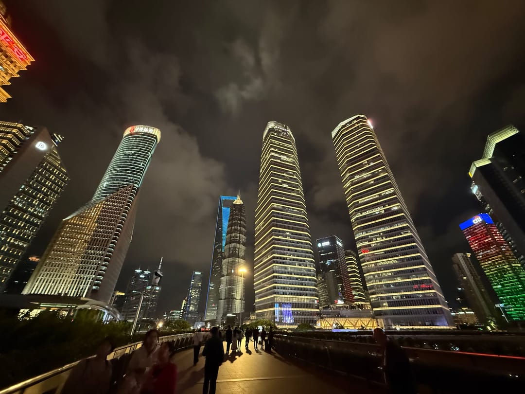 Gratte-ciel de Lujiazui illuminés la nuit vus depuis la passerelle piétonne circulaire, tour Jin Mao au centre et World Financial Center éclairé de bleu, promeneurs en contre-jour