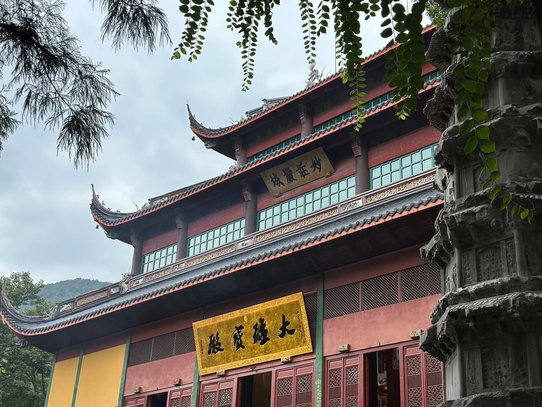 Hall du temple Lingyin à Hangzhou, mur jaune safran, plaque noire à caractères dorés et toiture à avant-toits relevés, branches de saule au premier plan