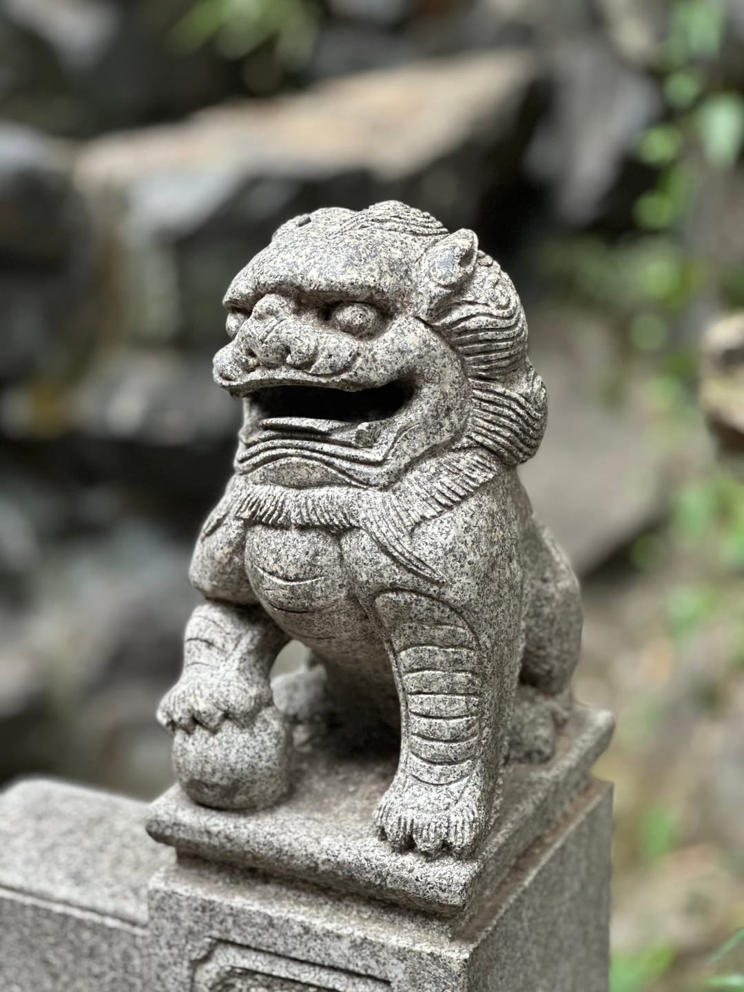 Lion gardien de pierre sculpté posé sur un socle à l'entrée d'un hall du temple Lingyin, pierre grise piquée de mousse