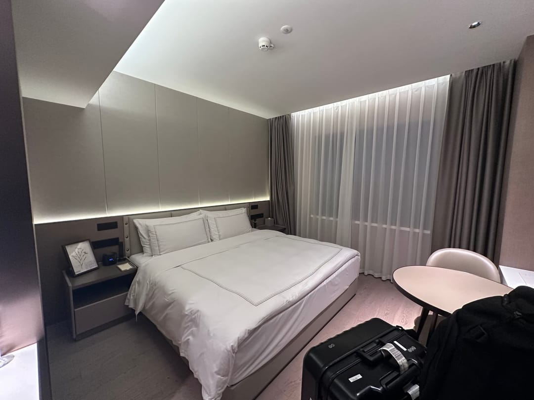 Chambre d'hôtel moderne à Shanghai, grand lit blanc, tête de lit rétroéclairée, rideaux jusqu'au sol et valise posée près du bureau
