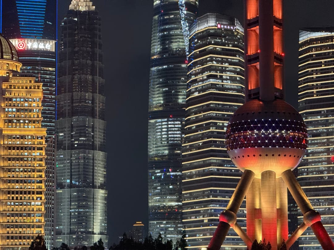 Skyline du quartier financier de Pudong à Shanghai de nuit, gratte-ciels illuminés en jaune et bleu, tour de la Perle de l'Orient avec sa boule rouge et violette éclairée à droite