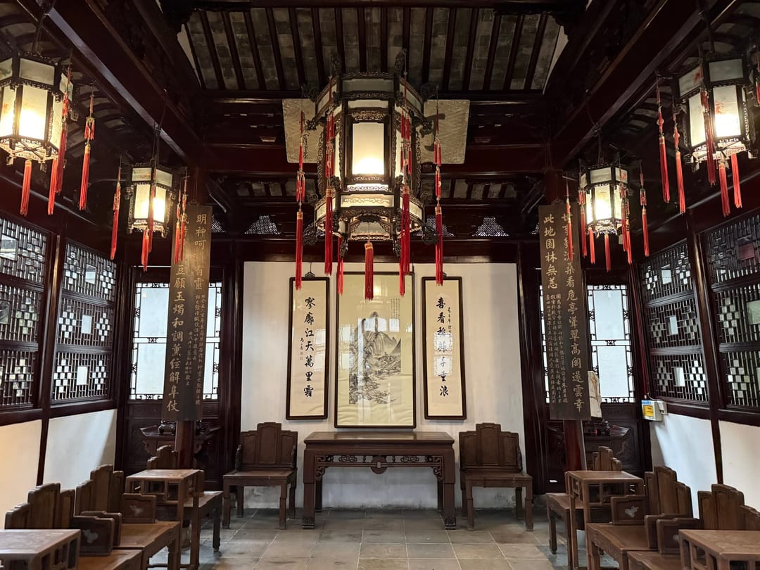 Salle de réception d'un jardin classique chinois, peinture encadrée au mur du fond, table d'autel, fauteuils de bois disposés en enfilade et lanternes suspendues