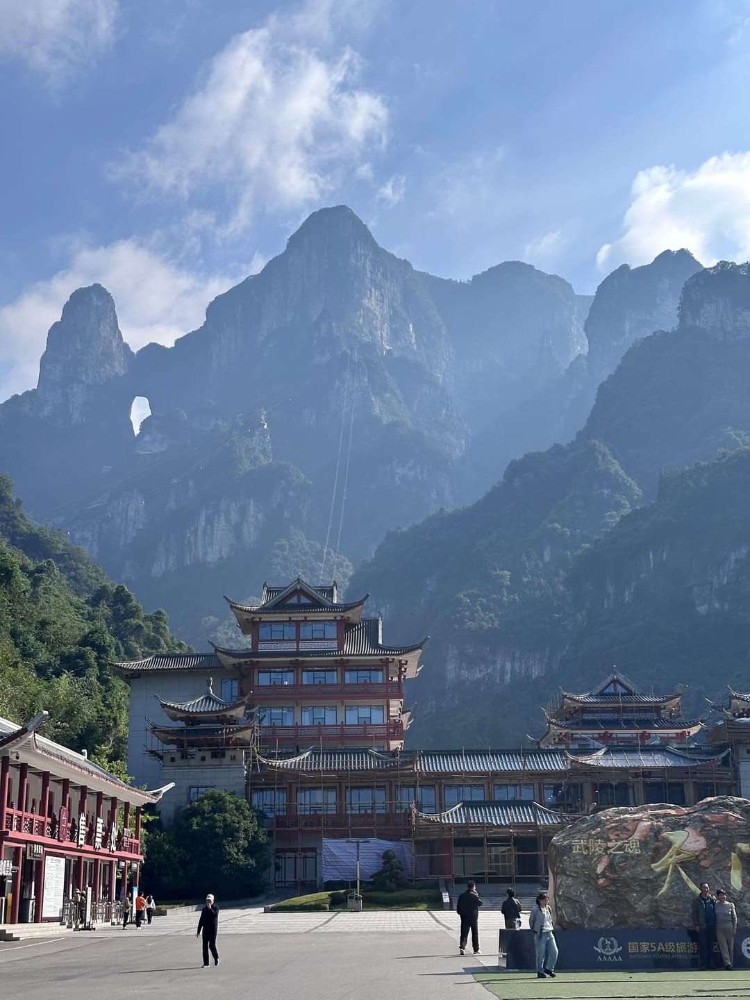 Esplanade du départ du téléphérique de la montagne Tianmen à Zhangjiajie, pavillons à toitures traditionnelles au pied des falaises, arche de la porte du Ciel visible sur la crête