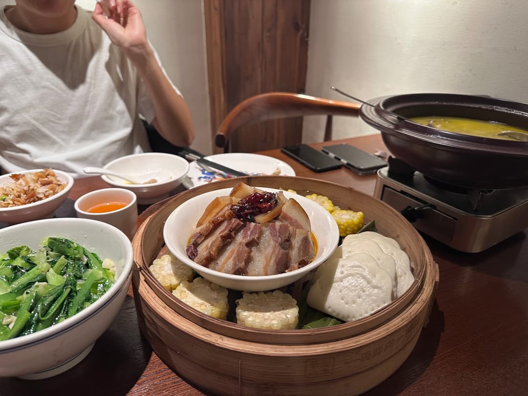 Table de restaurant du Hunan vue de dessus, bol de légumes verts, viande braisée en cocotte, pains vapeur et marmite sur réchaud