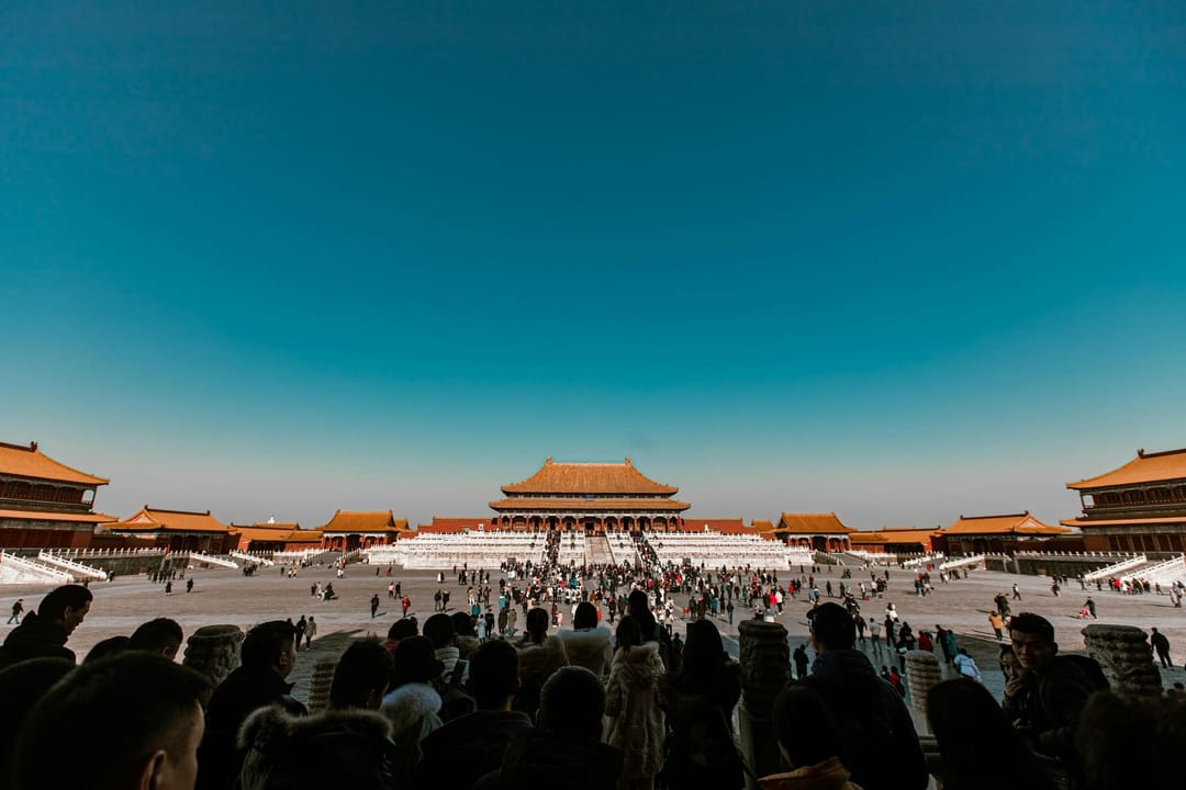 La Cité interdite à Pékin vue par-dessus une foule compacte au premier plan : têtes serrées de visiteurs en manteaux d'hiver, esplanade couverte de monde derrière eux et la salle de l'Harmonie suprême au fond sous un ciel bleu profond