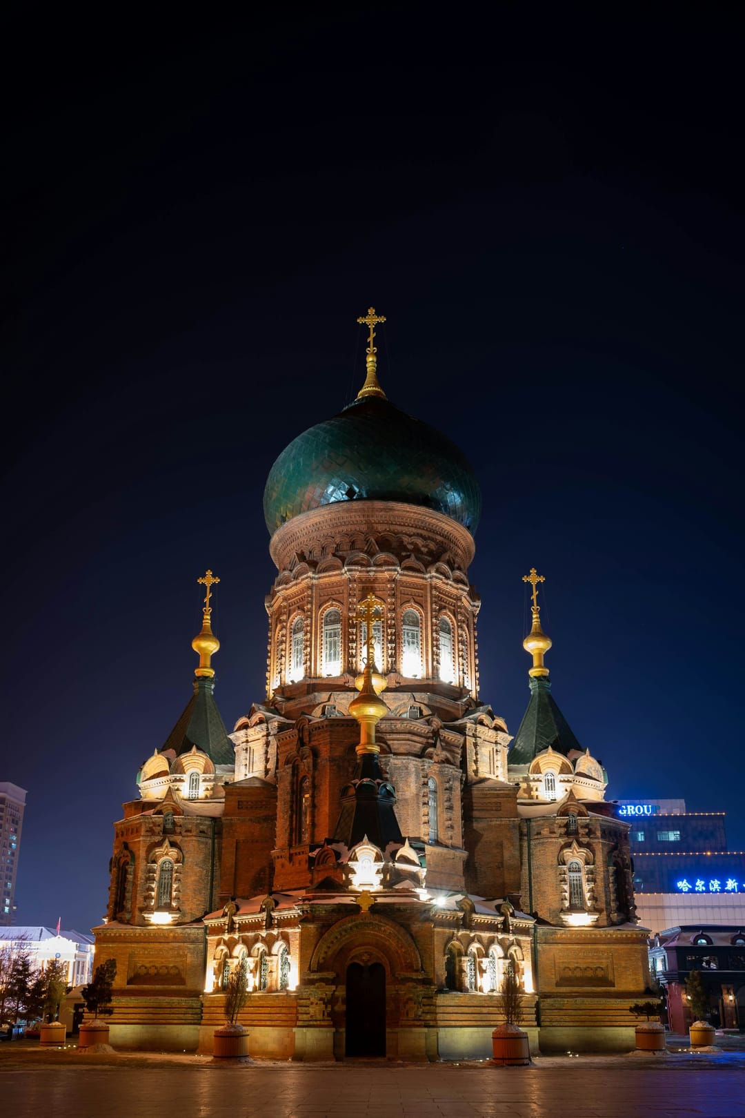 La cathédrale orthodoxe Sainte-Sophie de Harbin illuminée la nuit, briques rouges, grand bulbe vert et croix dorées, sous un ciel bleu nuit