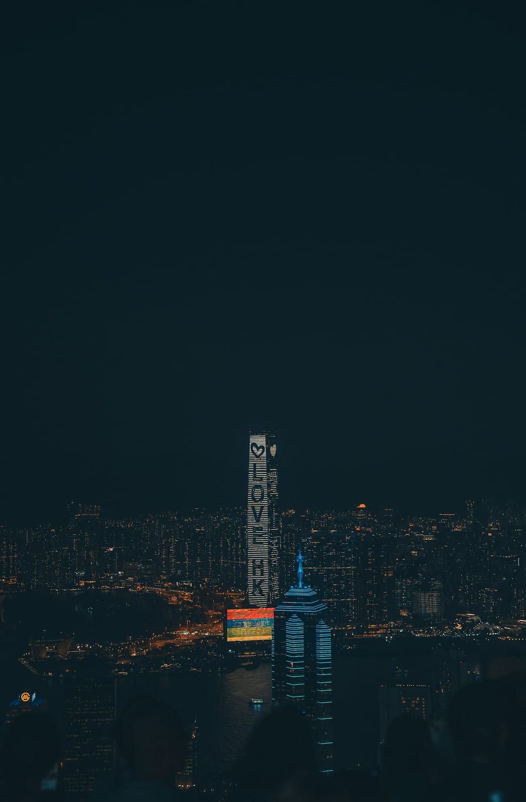 Gratte-ciel illuminés de Hong Kong la nuit vus depuis les hauteurs, tours serrées descendant vers le port de Victoria